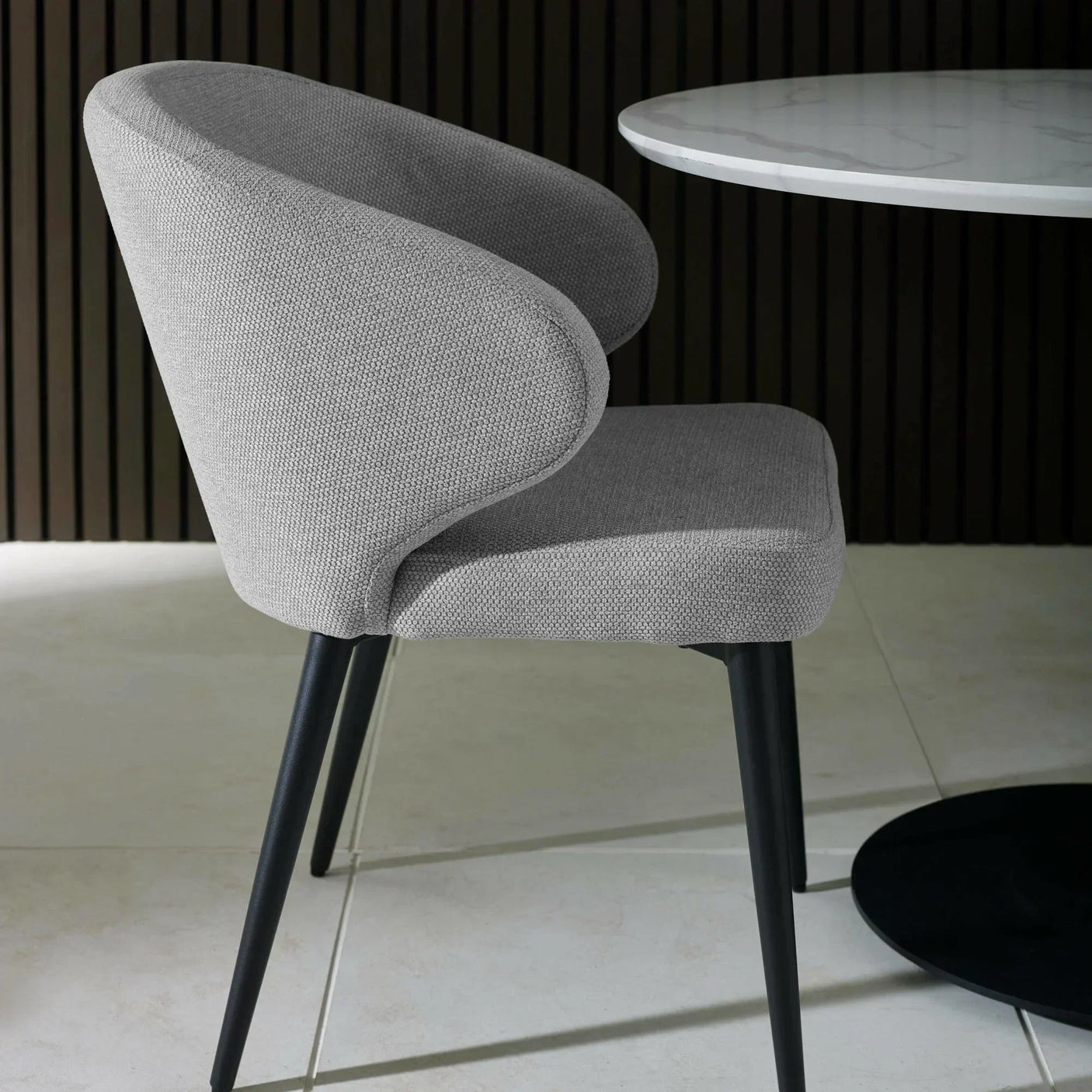 Grey fabric dining chair with curved backrest and black metal legs beside round table