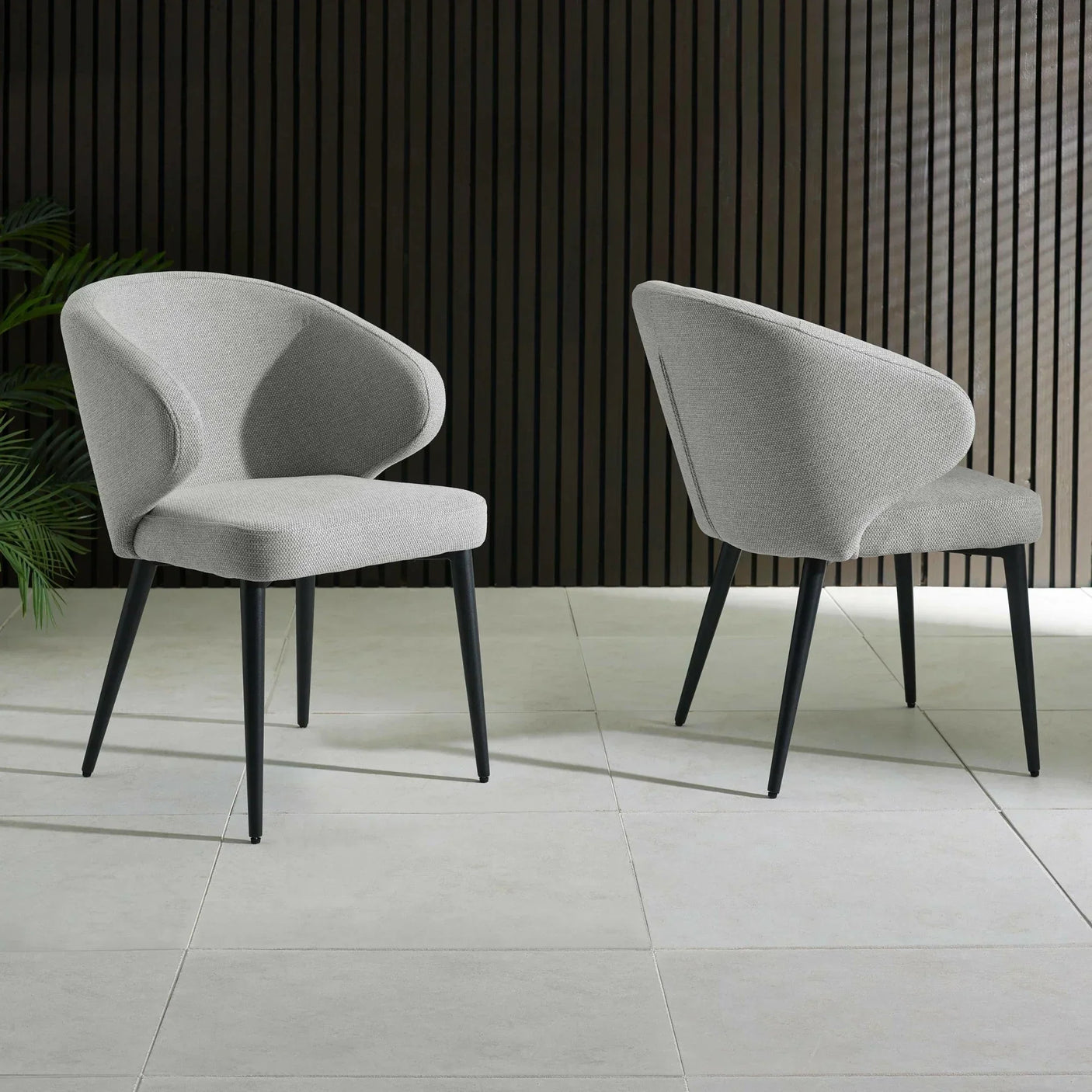 Pair of modern grey fabric dining chairs with curved backs and black legs on tiled floor