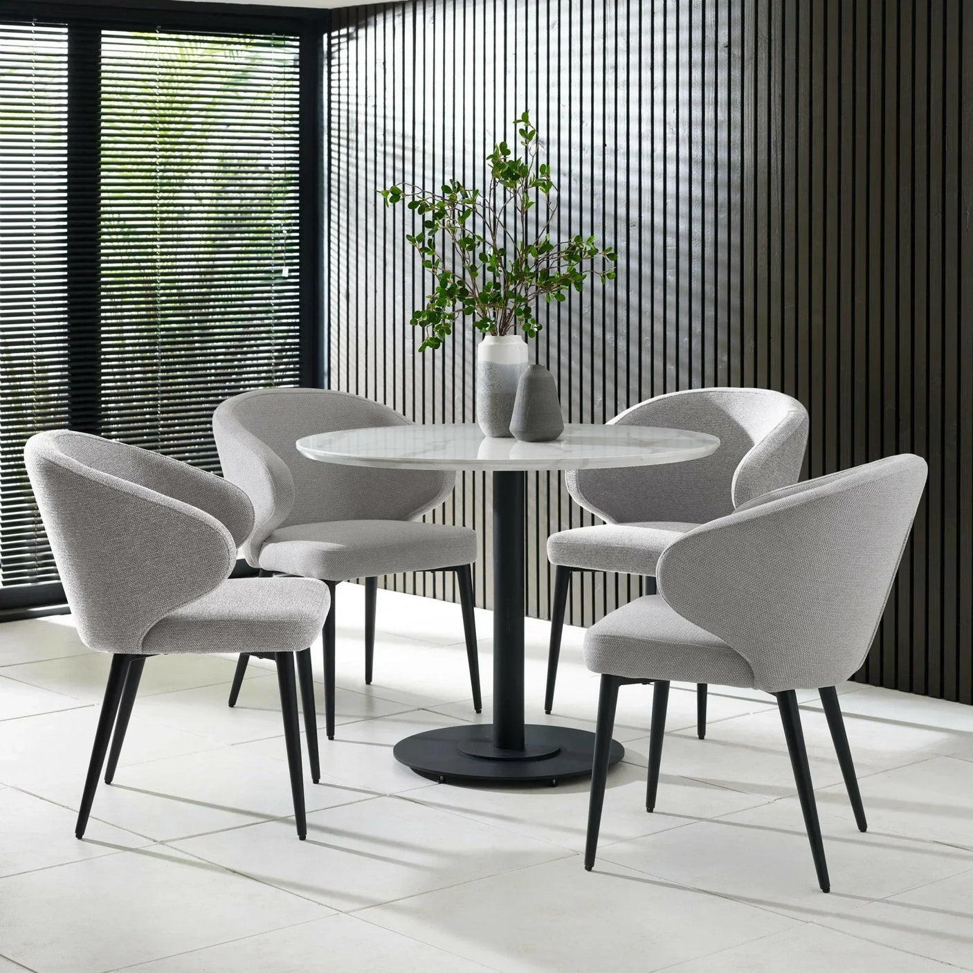 Modern grey dining set with round table and four fabric chairs on tiled floor
