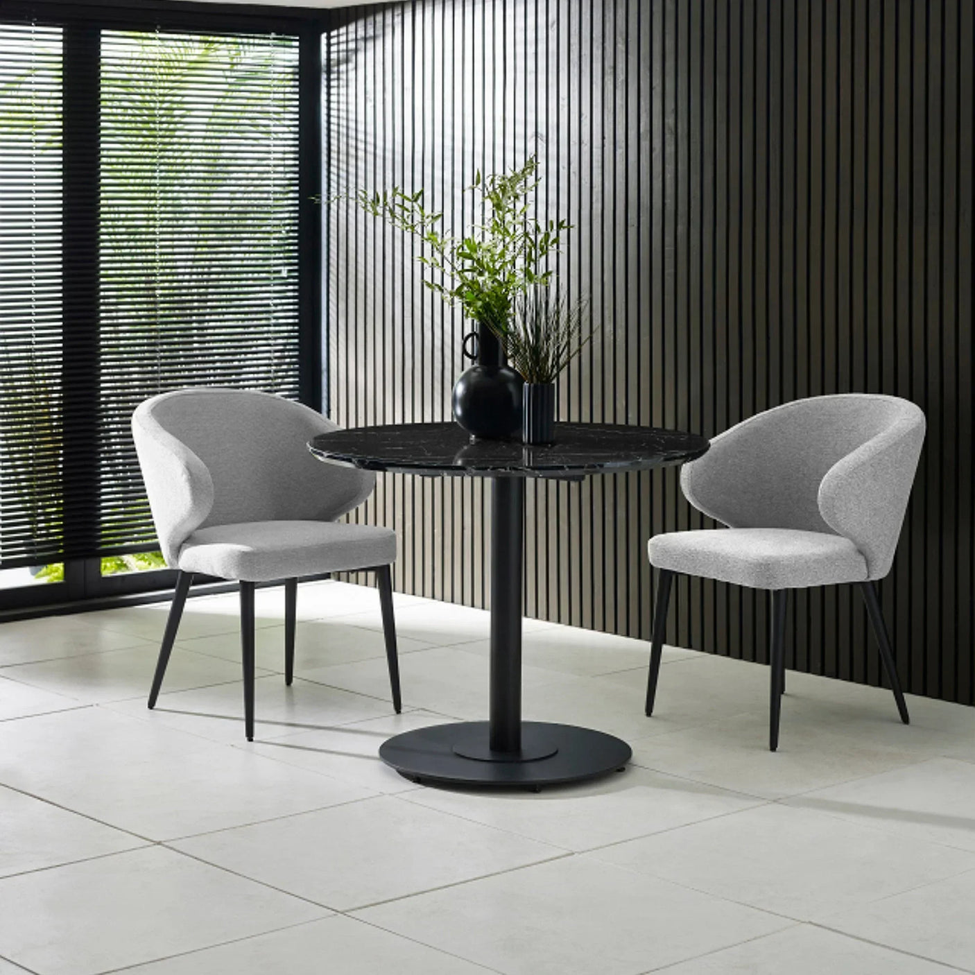 Round black dining table with grey fabric chairs in modern room with vertical slat wall