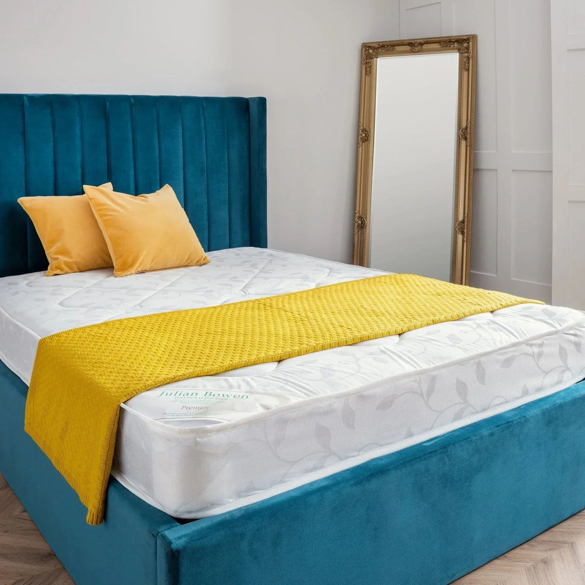 White quilted mattress on teal velvet bed base with mustard cushions and throw, bedroom setting