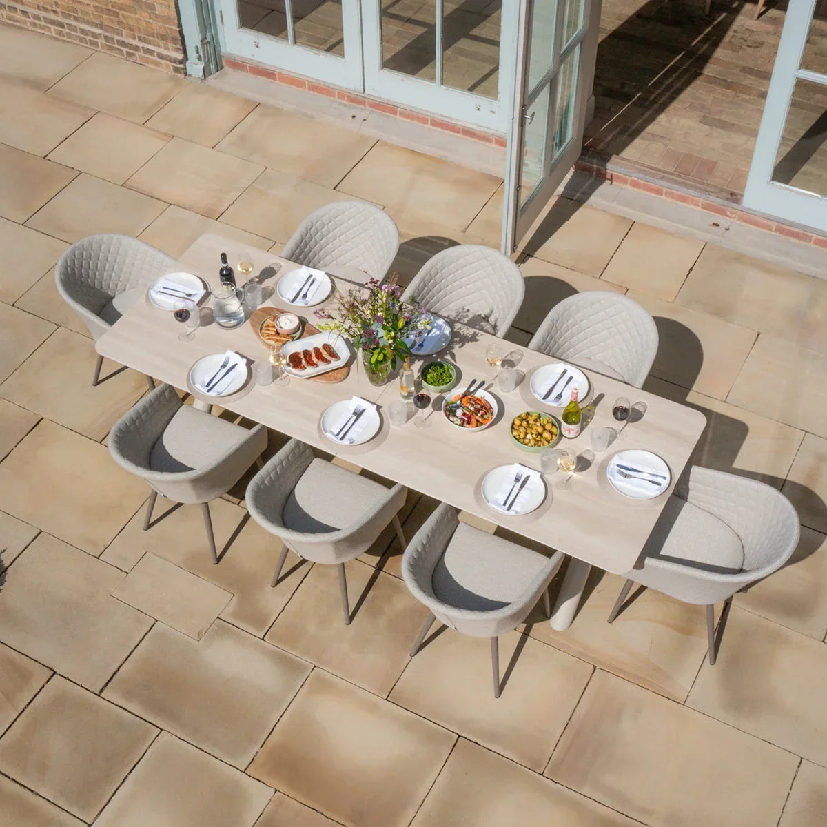 Beige outdoor dining set with eight cushioned chairs and rectangular table arranged for a meal