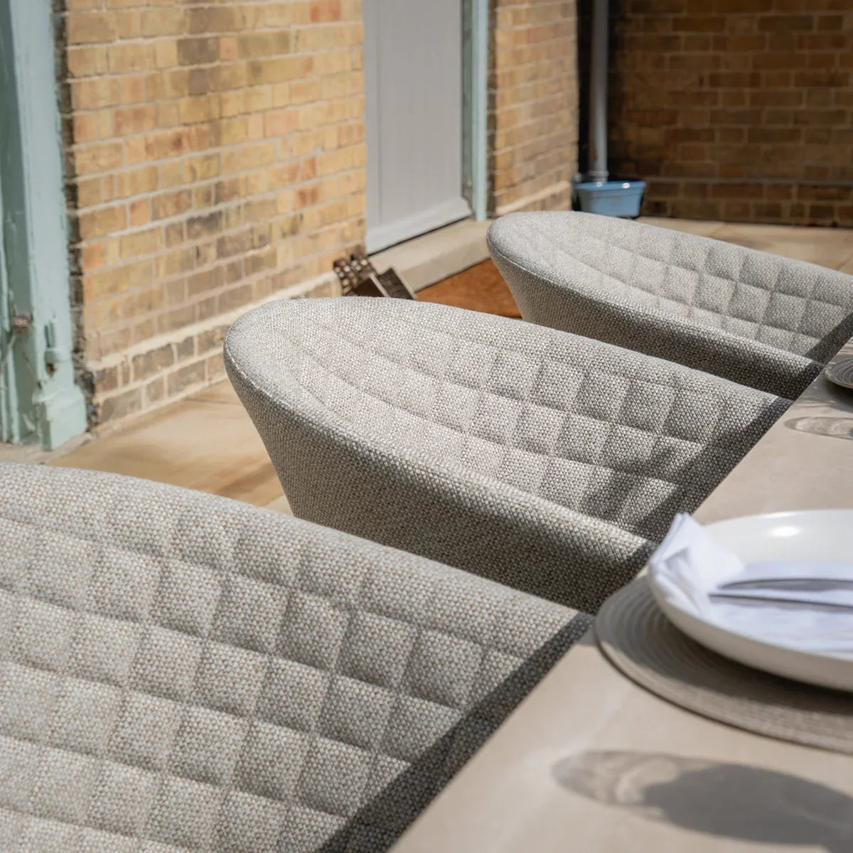 Light grey fabric dining chairs with quilted backs around outdoor table