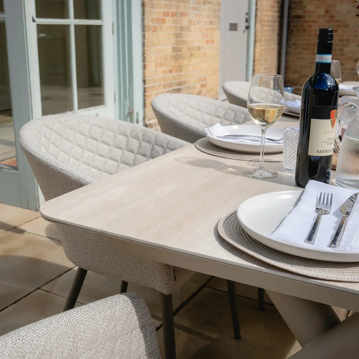 Light stone outdoor dining table set with cushioned chairs and tableware on patio