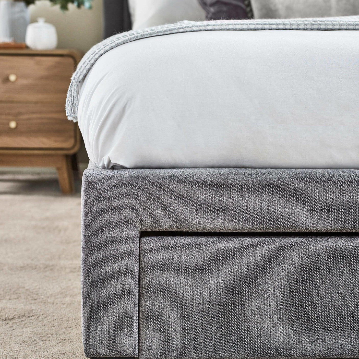 Grey upholstered bed frame with close-up of textured fabric next to wooden bedside table