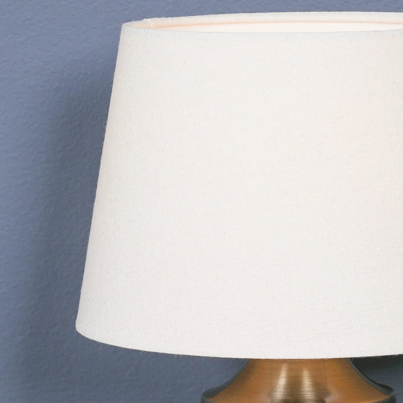Cream fabric lamp shade with brushed brass base against blue wall