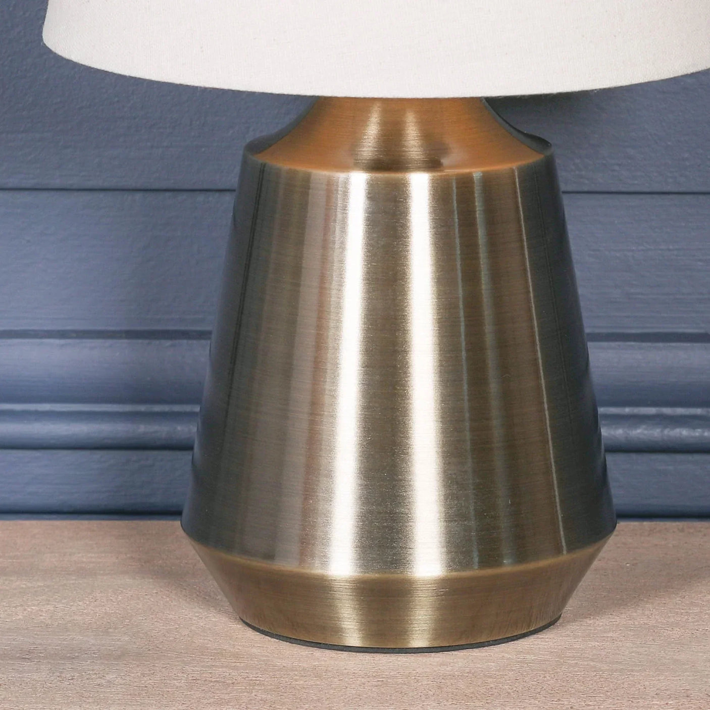 Brushed brass table lamp base with white fabric shade on wooden surface