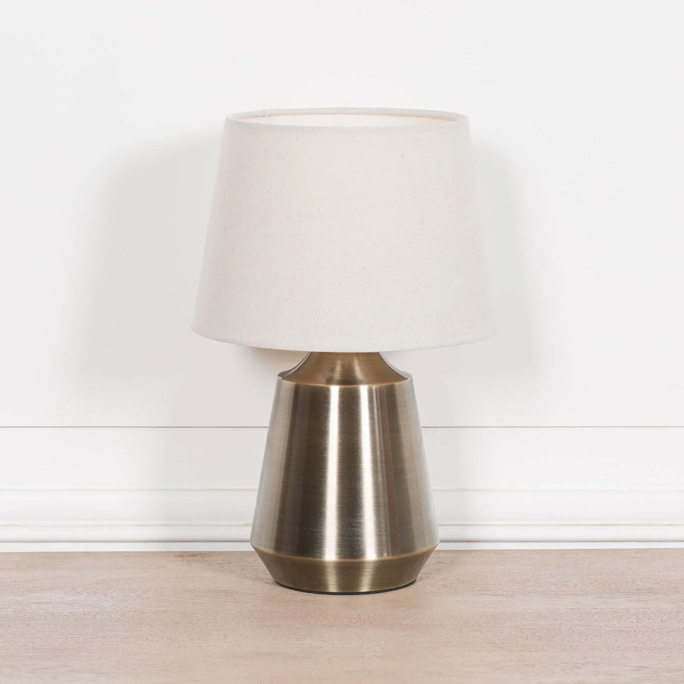 Brushed metal table lamp with cream fabric shade on wooden surface