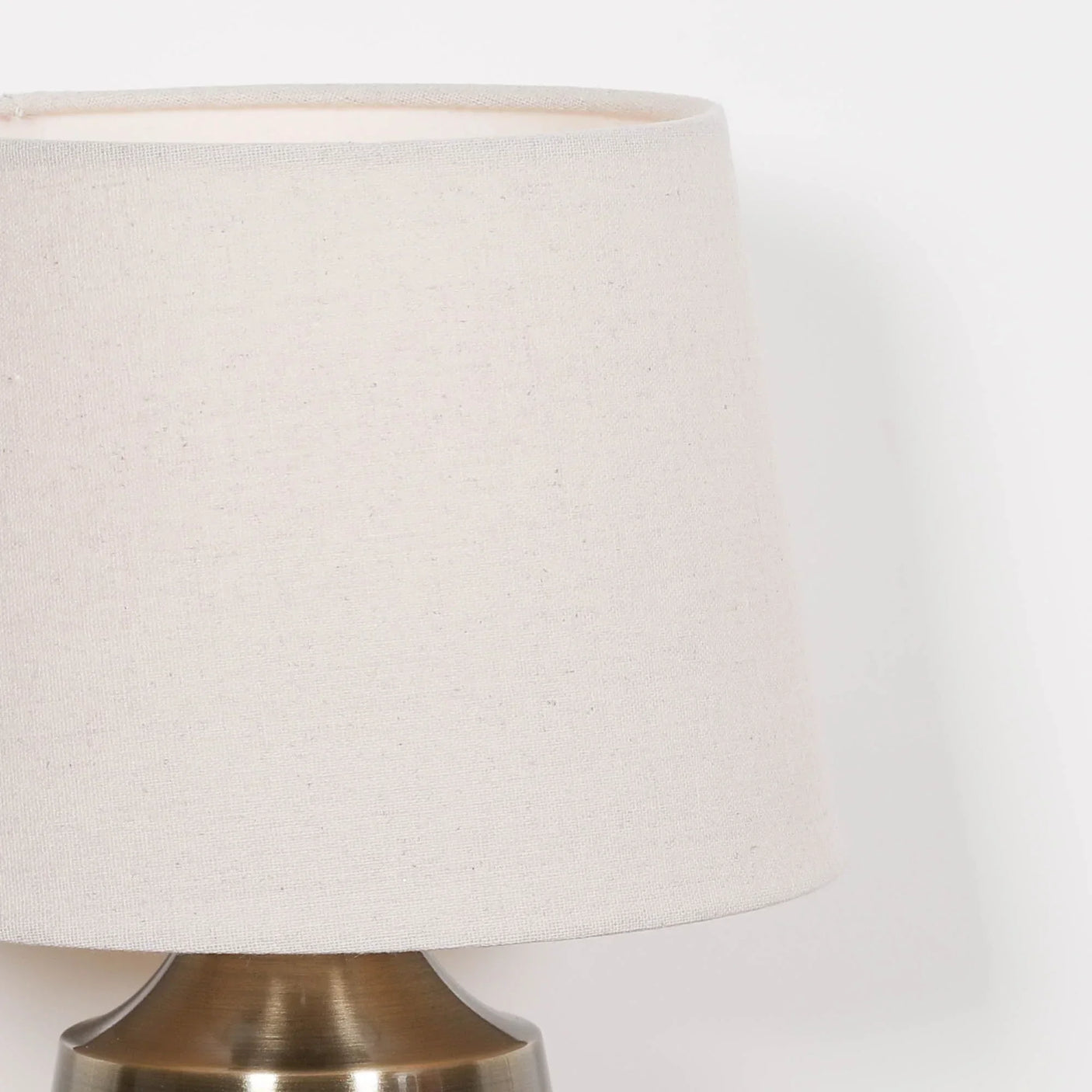 Cream fabric lampshade on brushed brass lamp base, close side angle