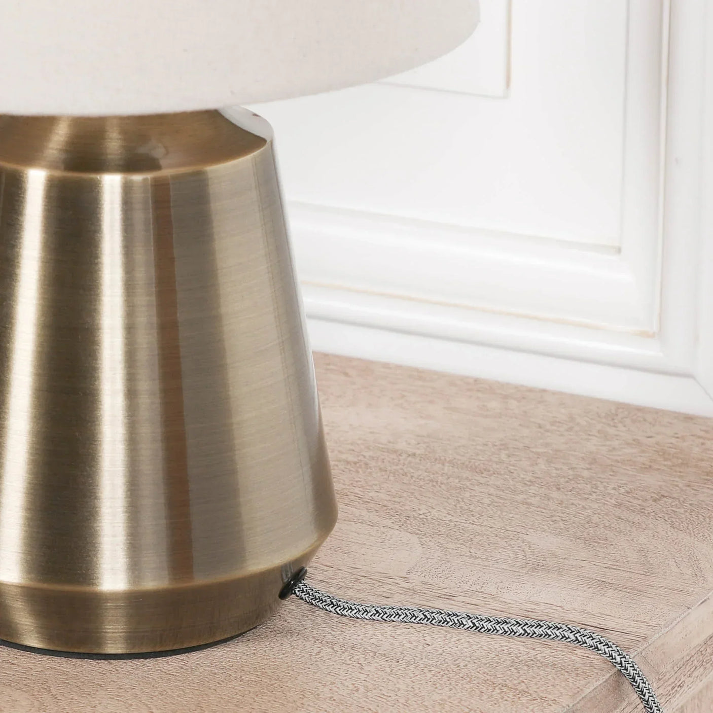 Brushed brass table lamp base with white fabric shade on wooden surface