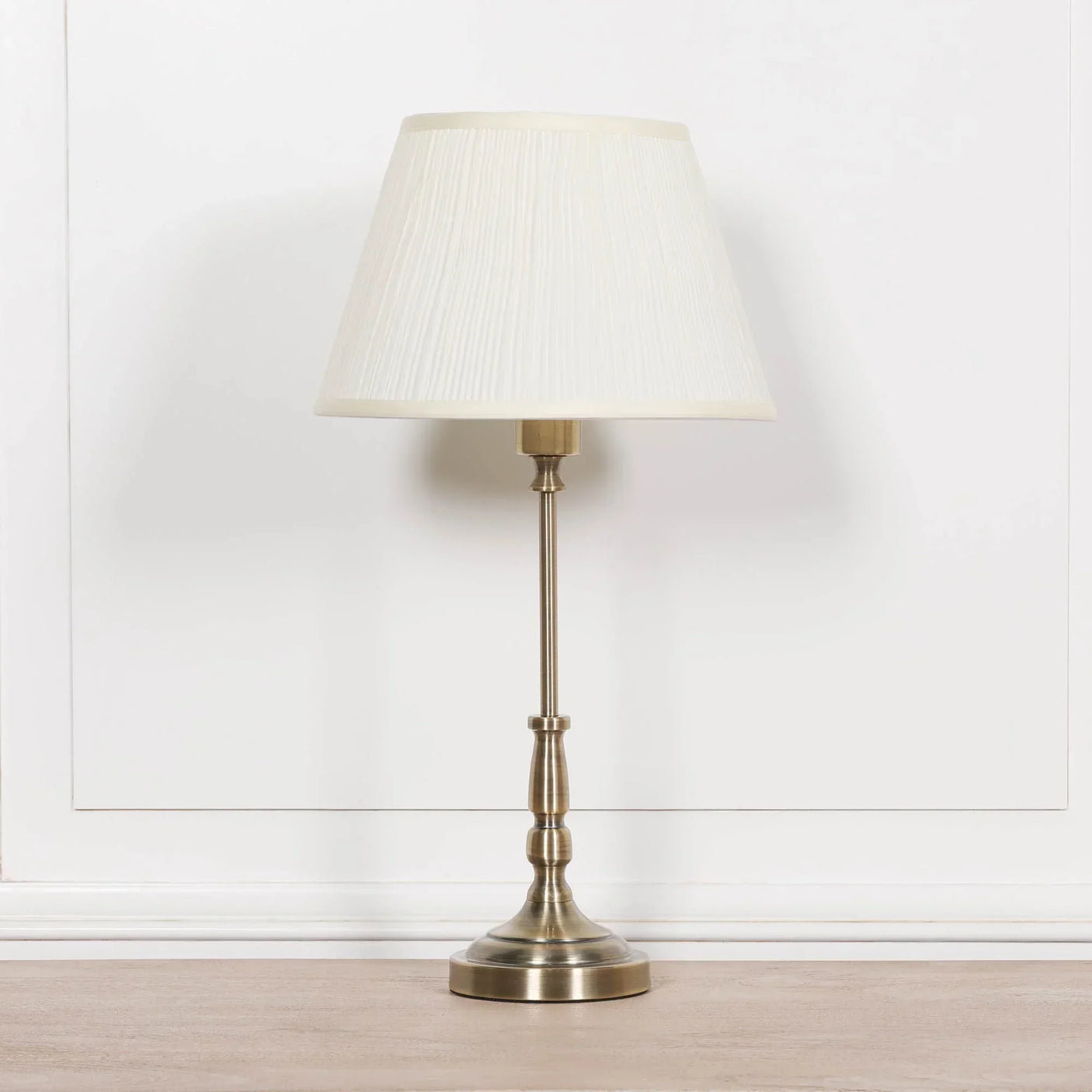 Brass table lamp with pleated white fabric shade on wooden surface against white wall