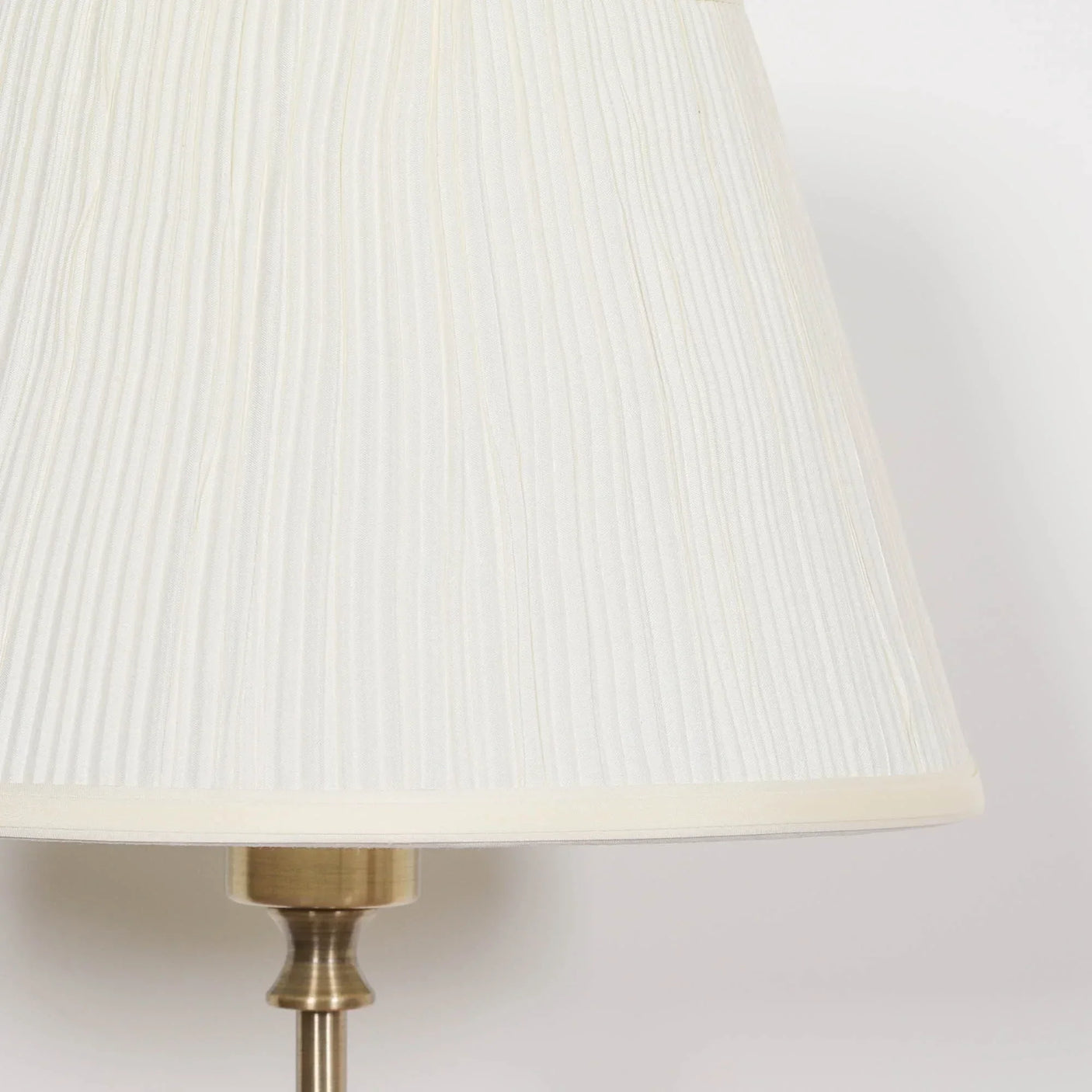 Cream pleated lampshade with brass lamp base detail on white background