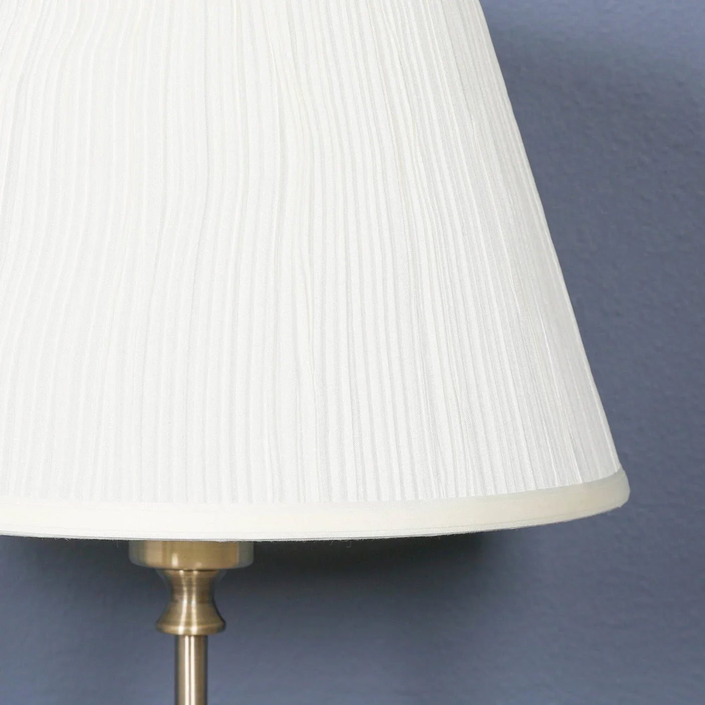 Cream pleated fabric lamp shade with brass base against blue wall