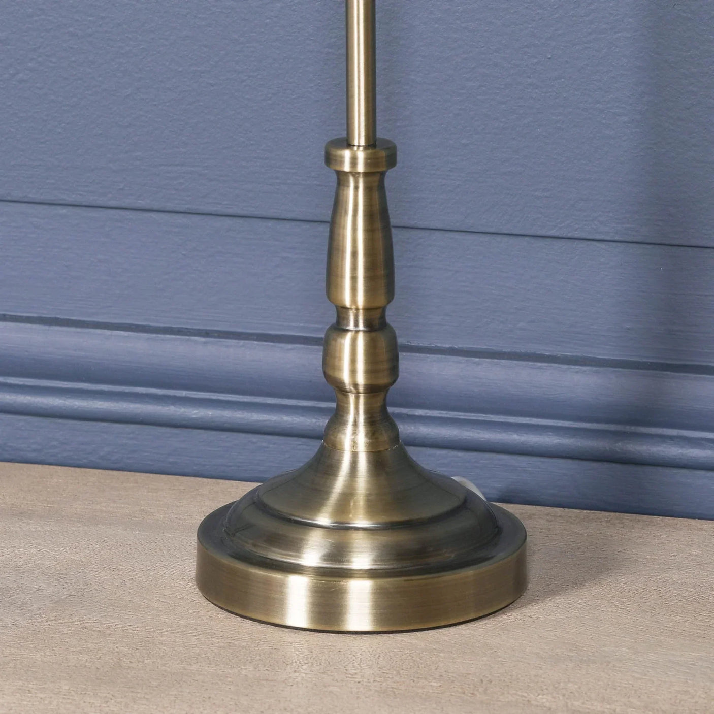 Brushed brass lamp base with turned detailing on wooden table against blue wall