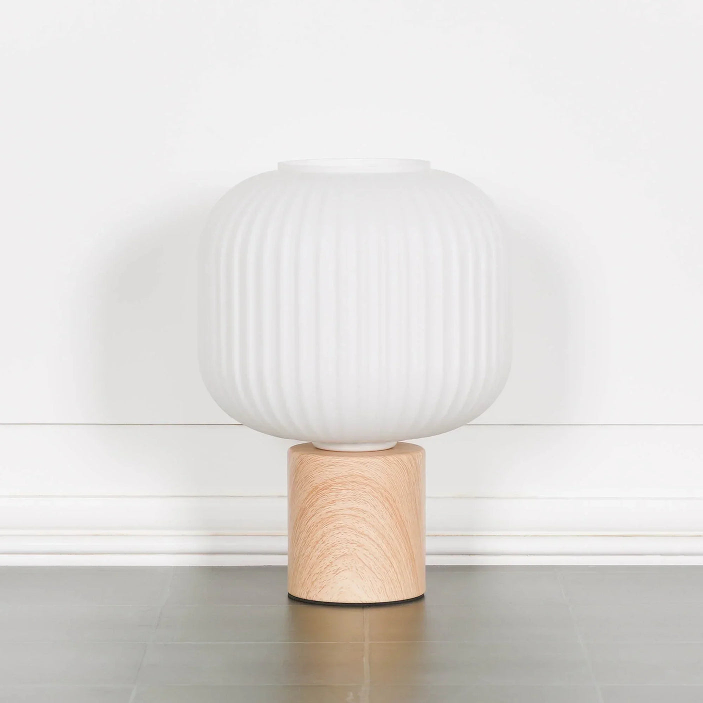 White ribbed glass table lamp with natural wood base on grey floor