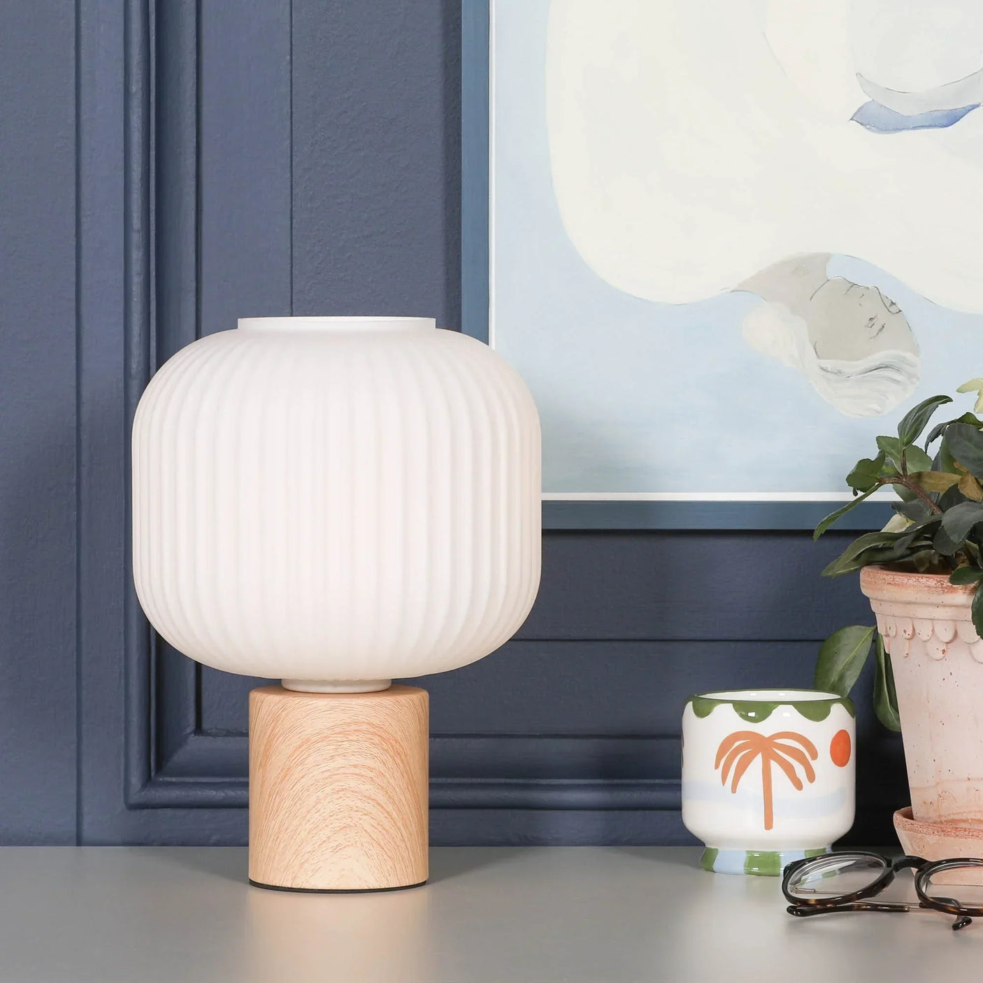 Modern table lamp with ribbed white glass shade and wooden base on grey surface