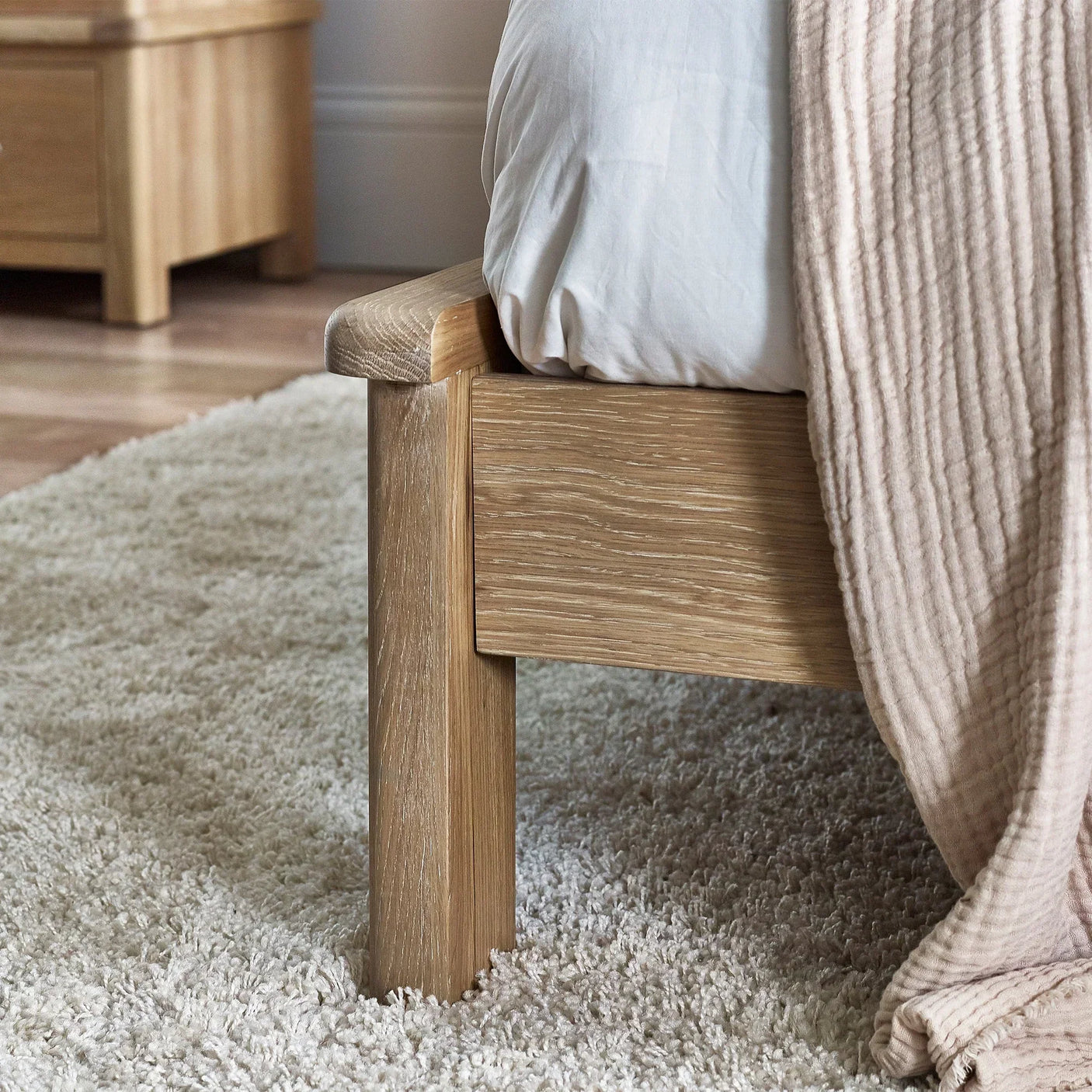 Close-up of limed oak bed frame with textured wood grain on cream carpet