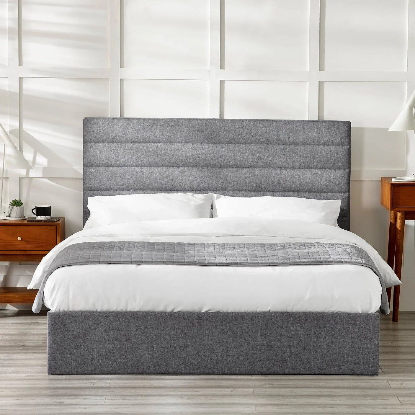 Grey upholstered storage bed with tall headboard, white bedding, wooden bedside tables