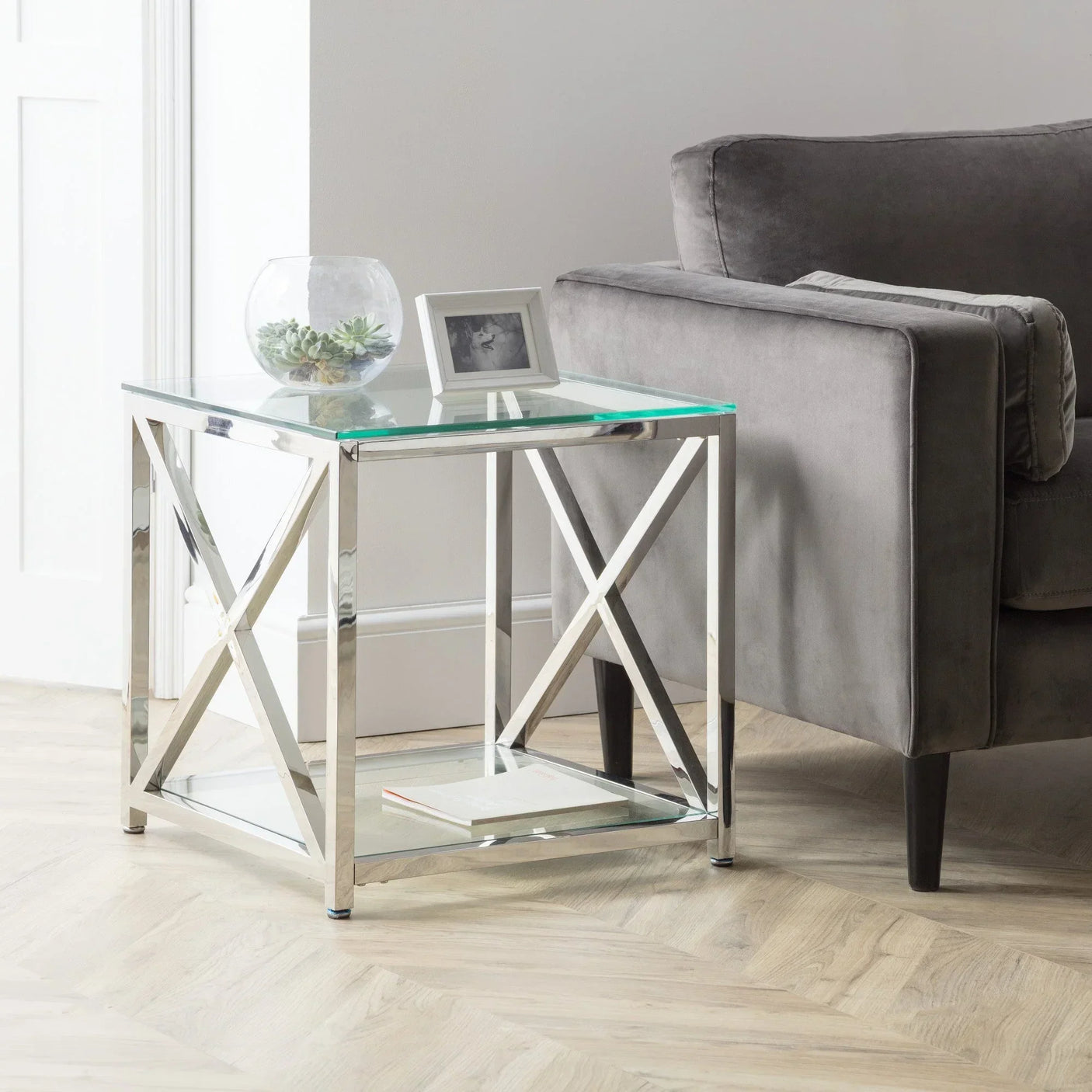 Glass side table with chrome frame beside grey sofa in modern living room setting