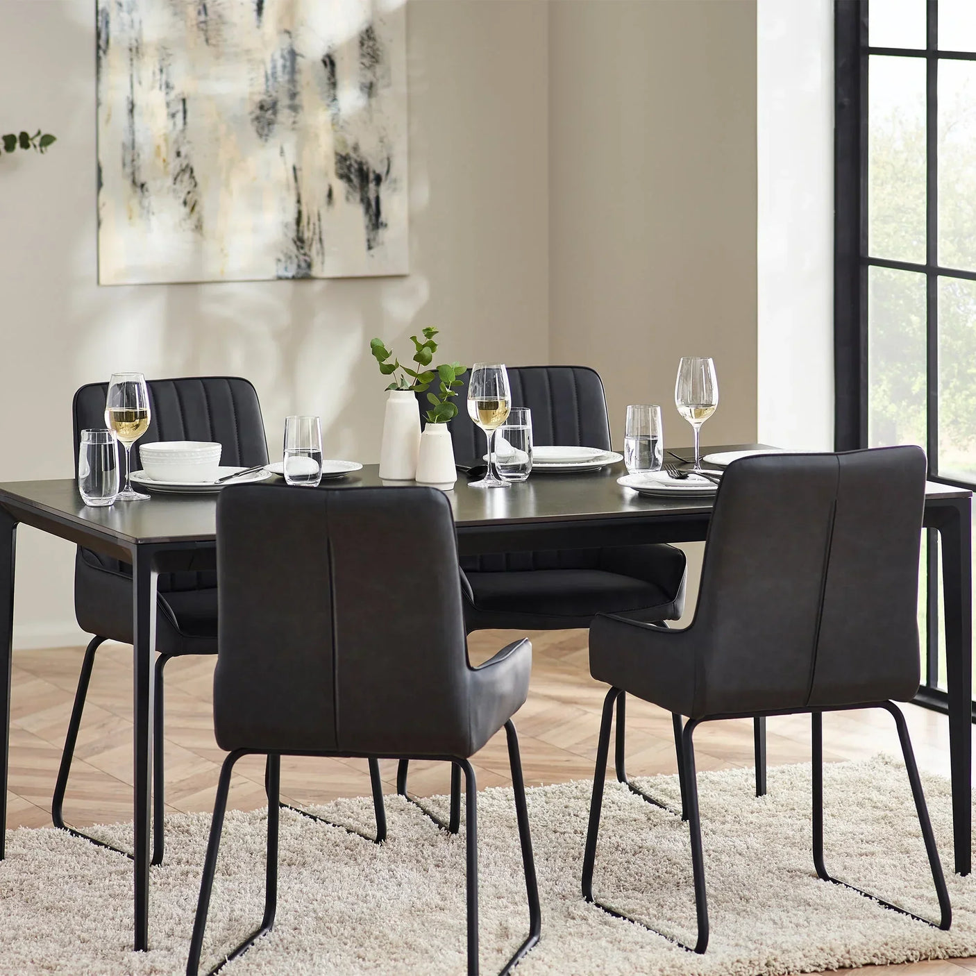 Rectangular stone top dining table with black chairs set for four in modern dining room
