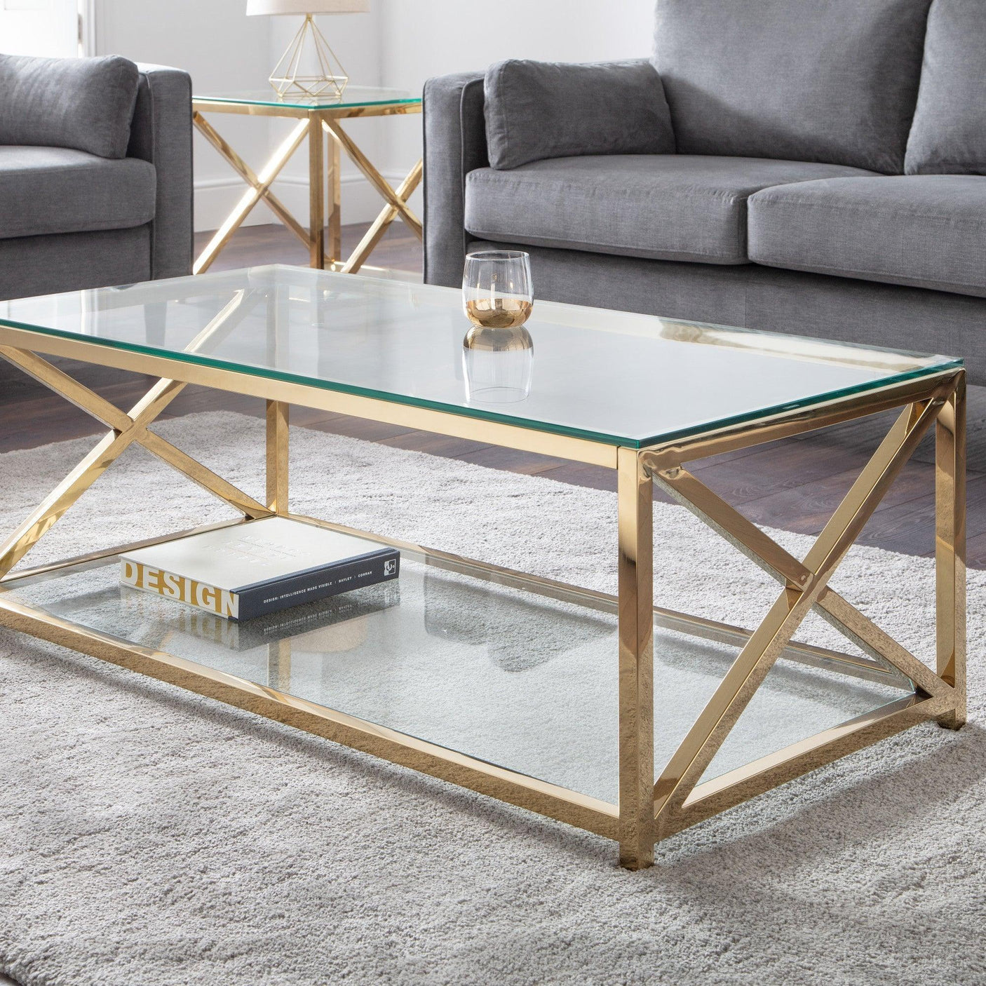 Glass coffee table with gold metal frame on grey rug, styled with book and candle, living room setup
