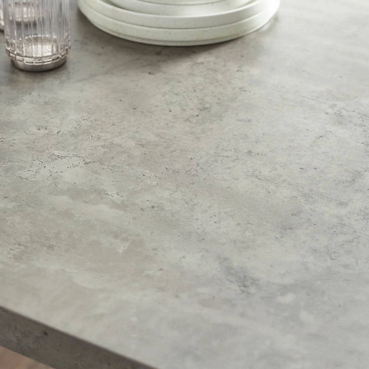 Concrete effect dining table top surface with textured grey finish, glass and stacked plates
