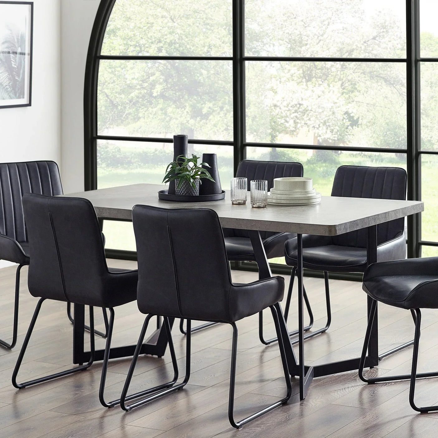 Concrete effect dining table with black metal legs and six black chairs in modern dining room