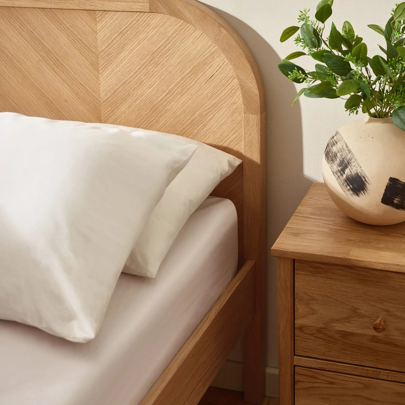oak bed frame and matching bedside table with white bedding and ceramic vase with greenery