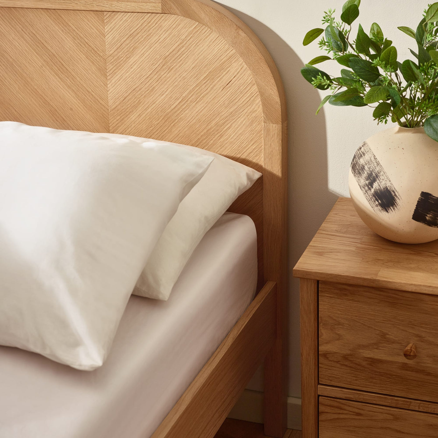 Close-up of curved oak headboard corner beside bedside table and vase