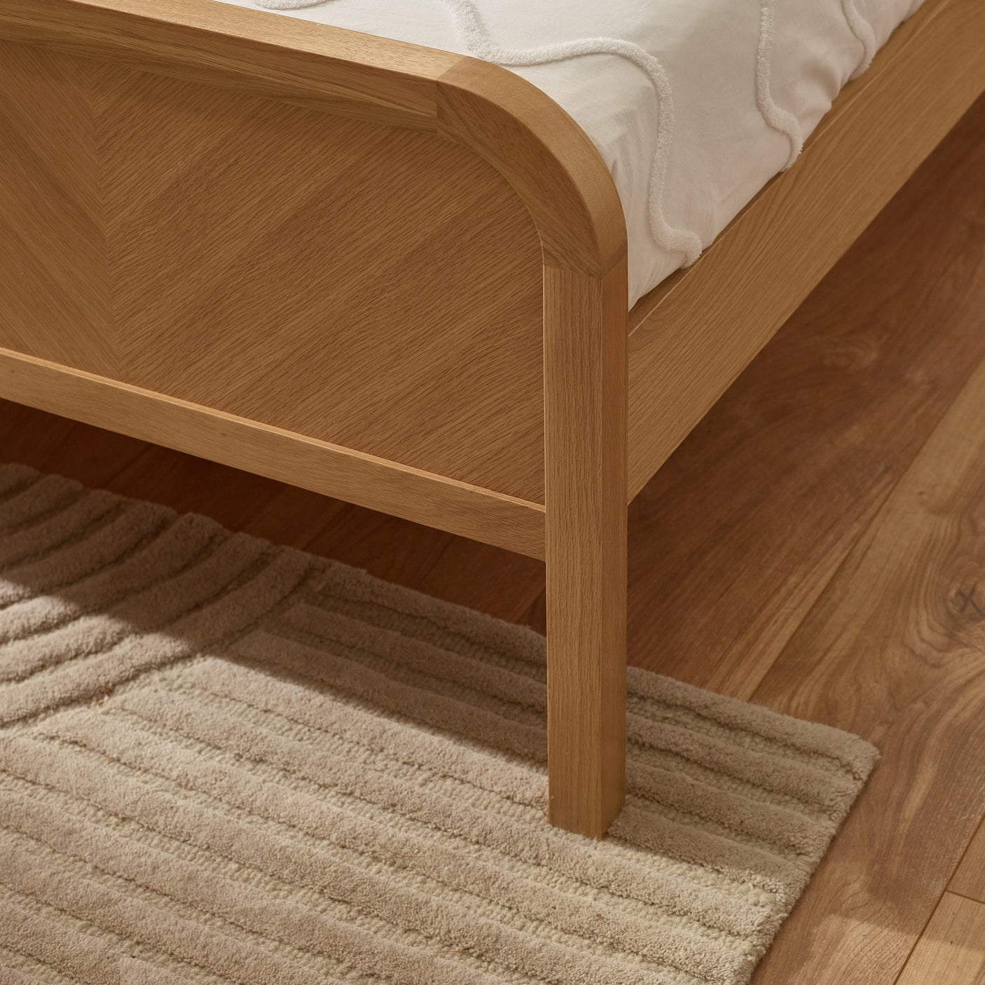Close-up of light oak bed frame corner and leg on a woven rug