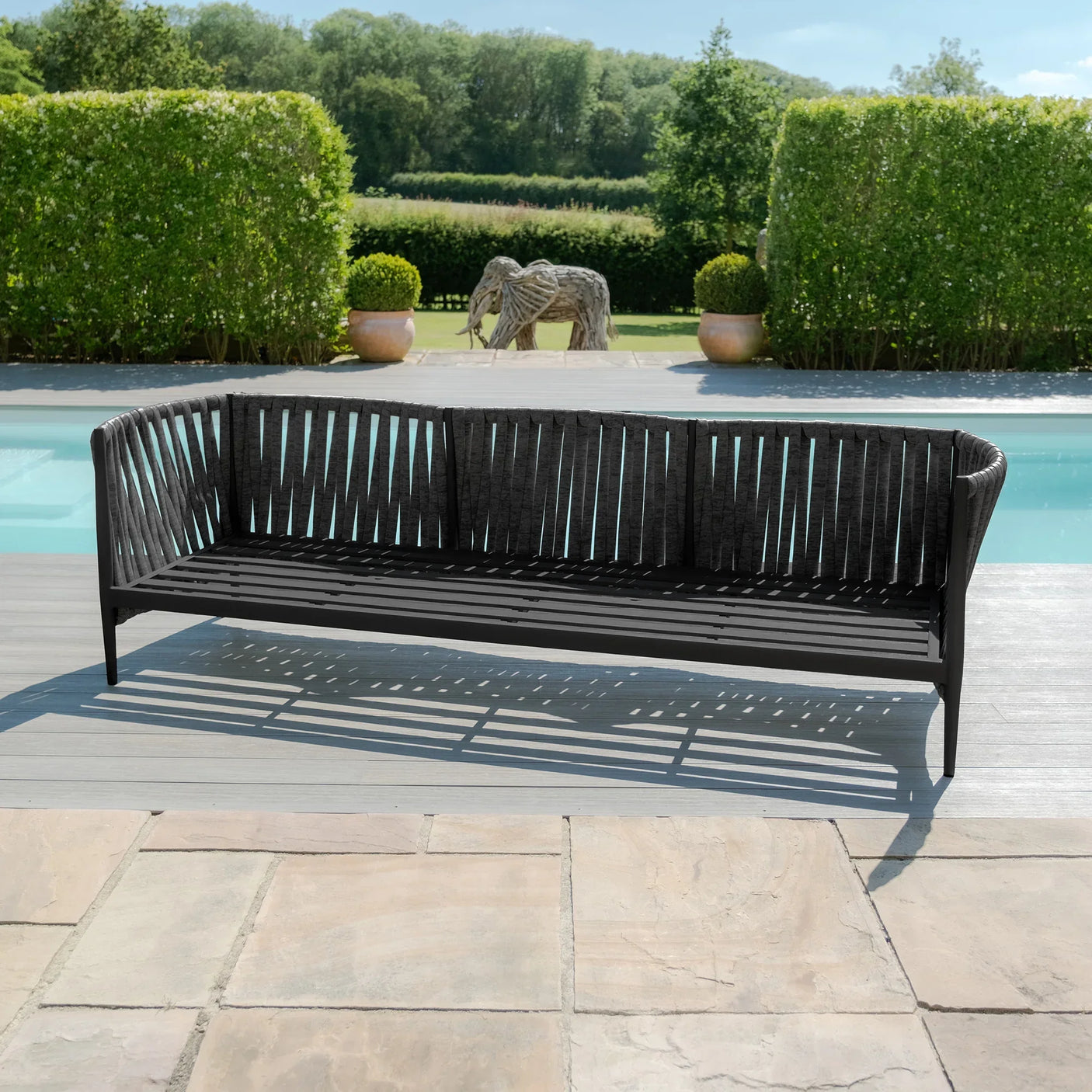 Black rope outdoor sofa on patio beside pool with greenery in background