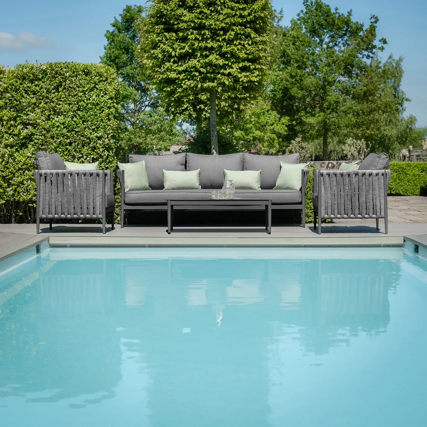 Grey outdoor furniture set with sofa, armchairs and coffee table by pool on patio