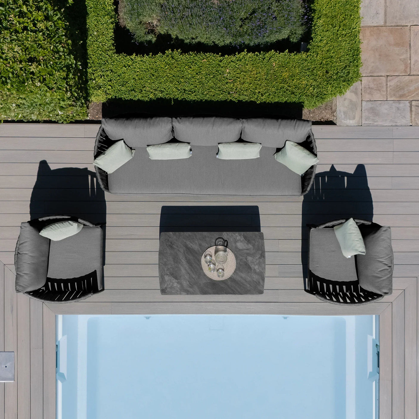 Grey outdoor sofa set with matching armchairs and low table by pool on deck