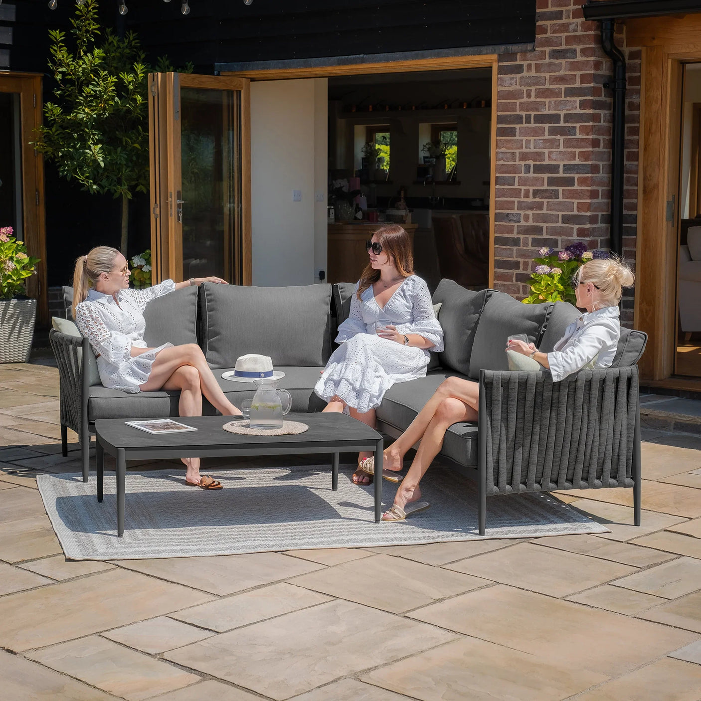 Grey outdoor corner sofa set with coffee table and three women relaxing on patio