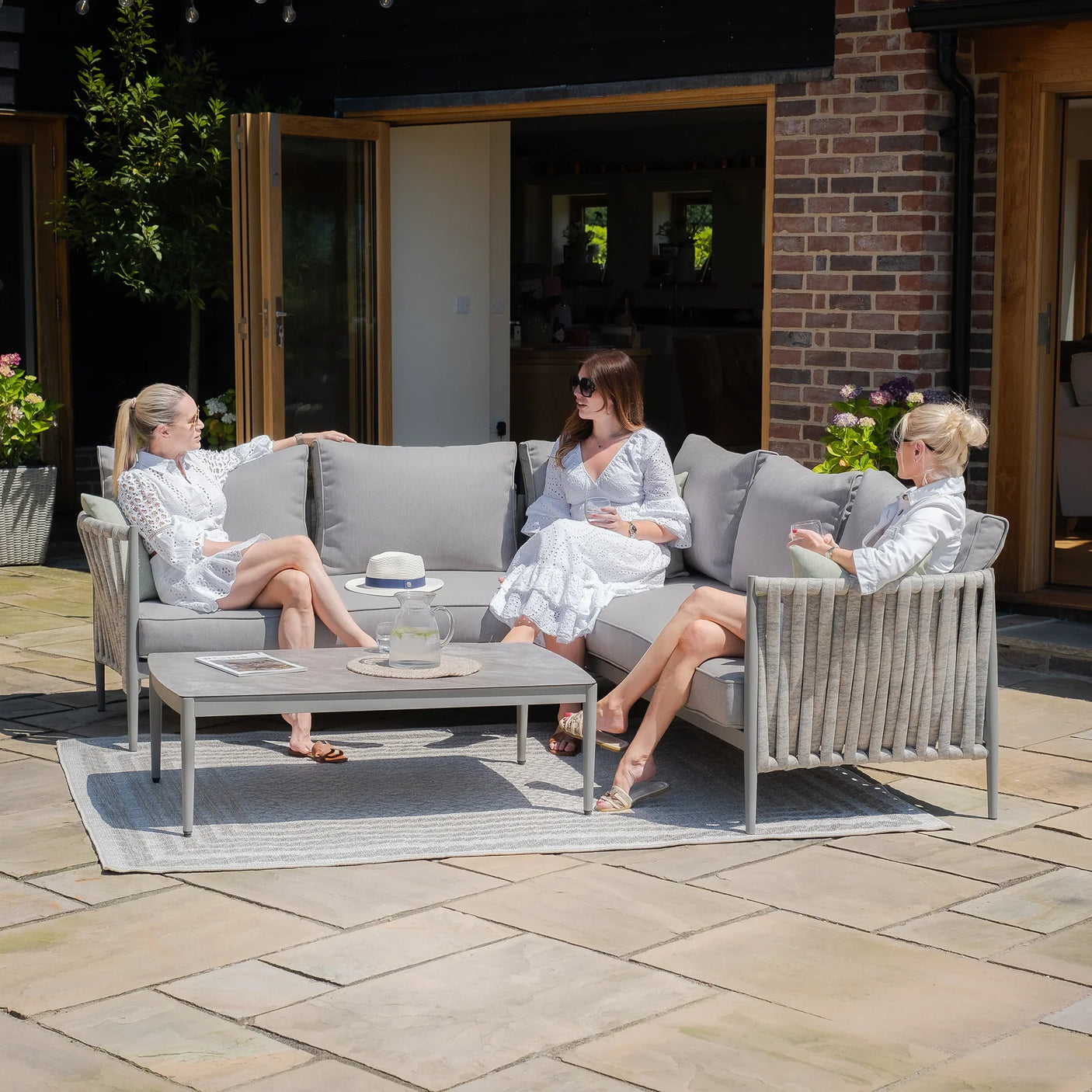 Grey outdoor sofa set with cushions and coffee table on patio, three women seated in garden