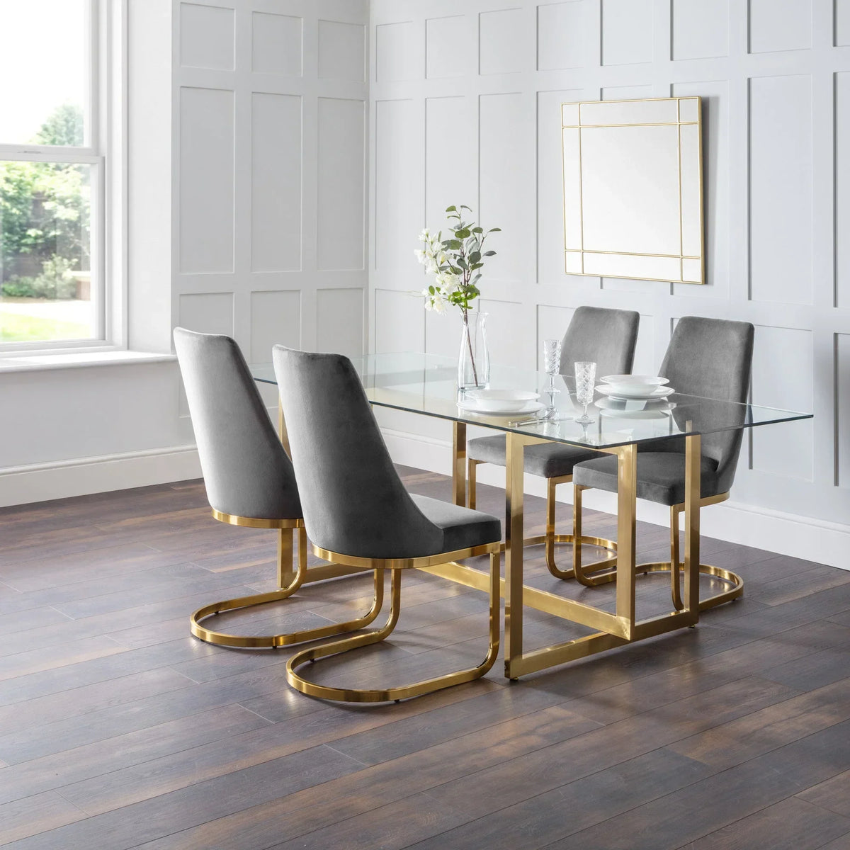 Glass dining table with gold metal legs and grey velvet chairs in modern dining room