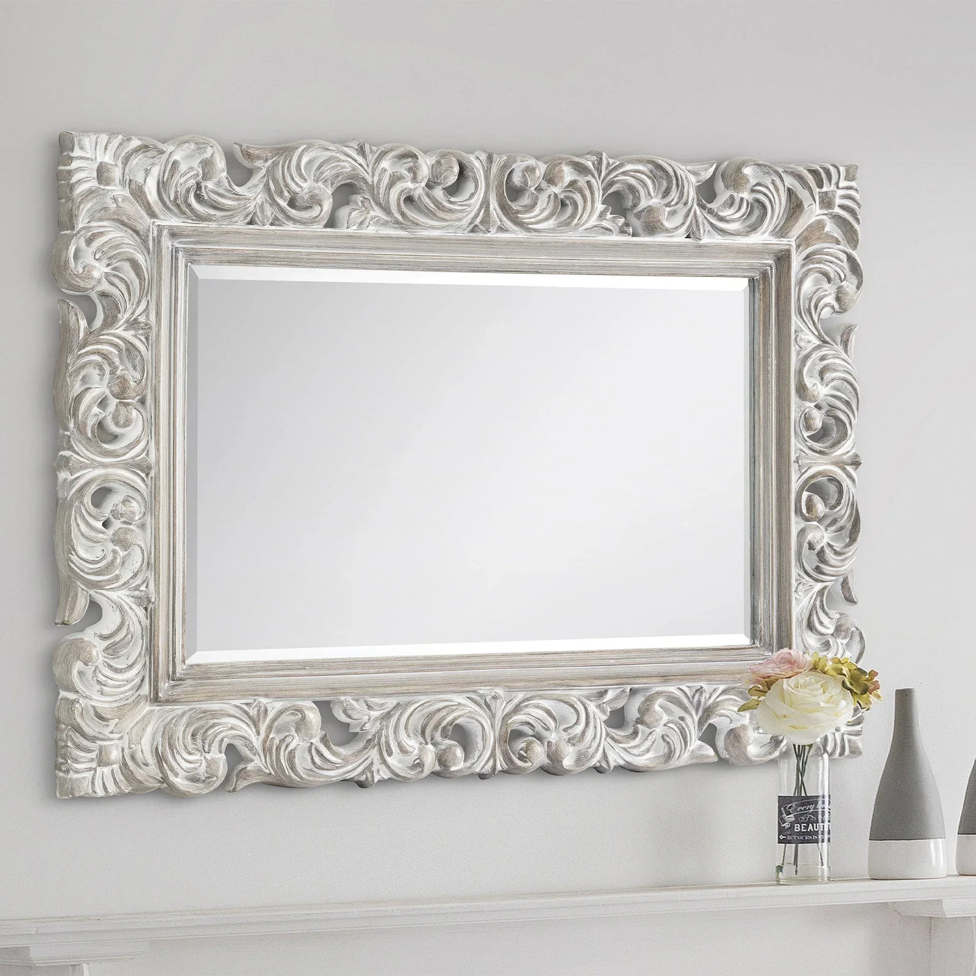 Baroque distressed wall mirror with ornate silver frame above shelf and floral decor