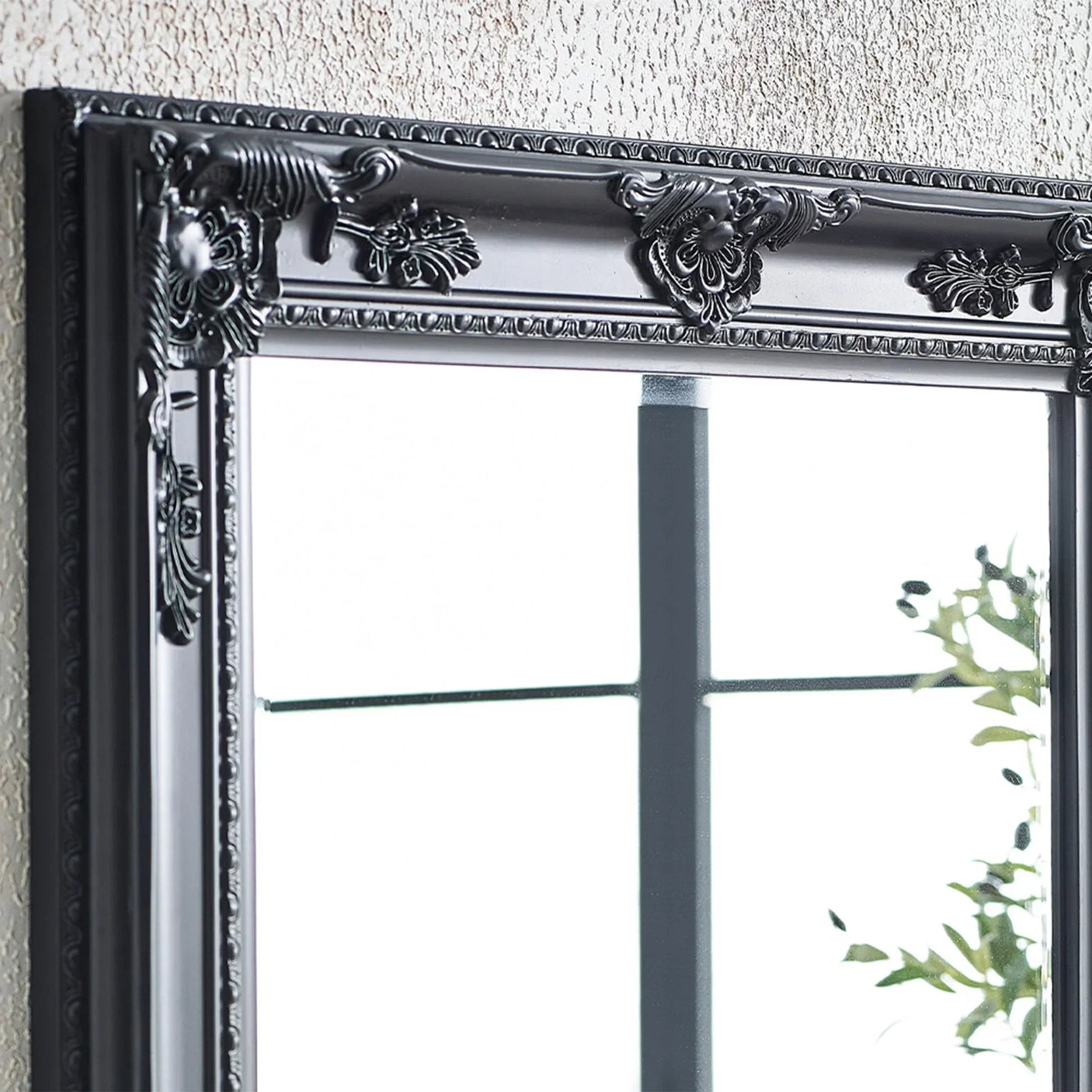 Black ornate mirror frame with decorative floral detailing against textured wall