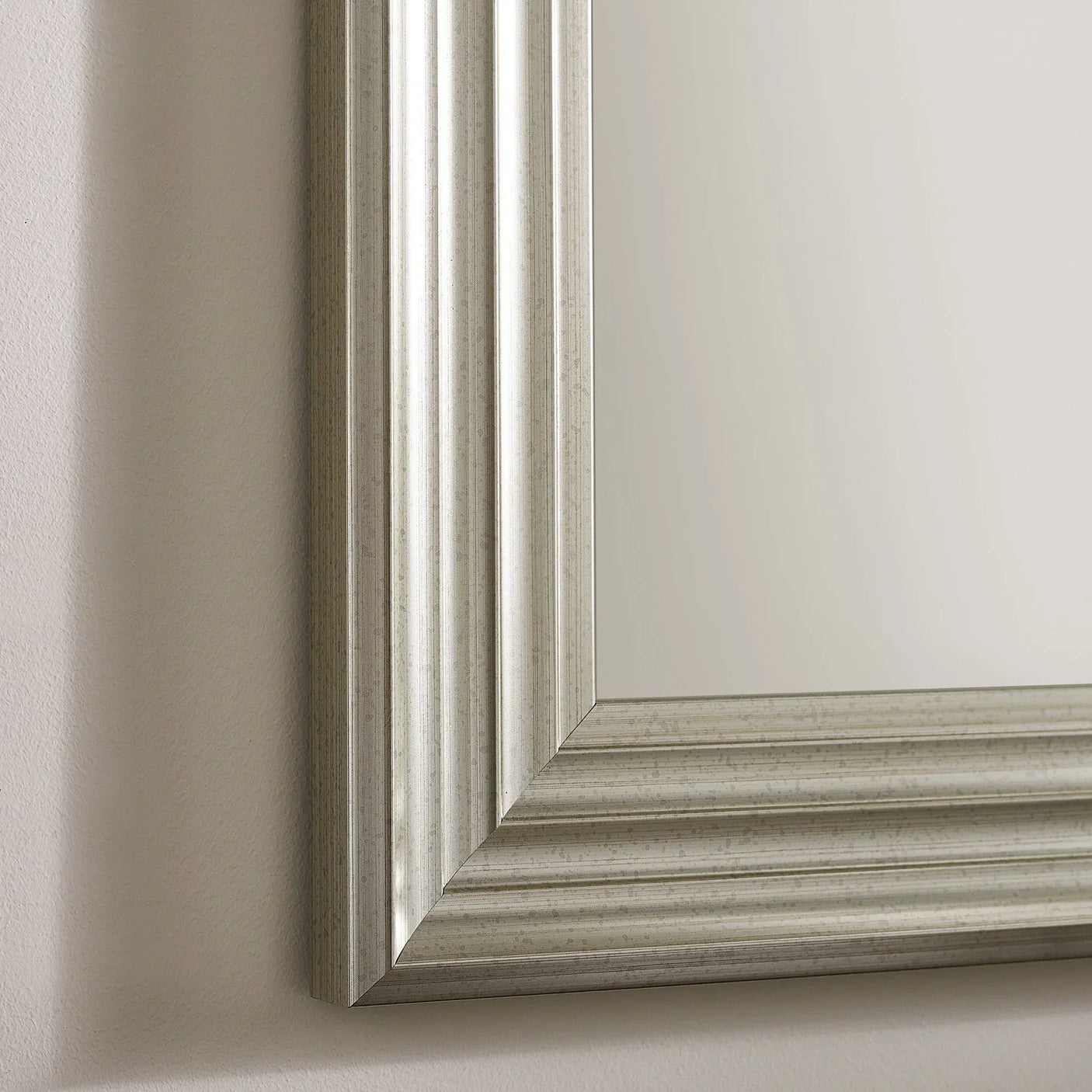 Silver wall mirror with grooved rectangular frame on beige wall