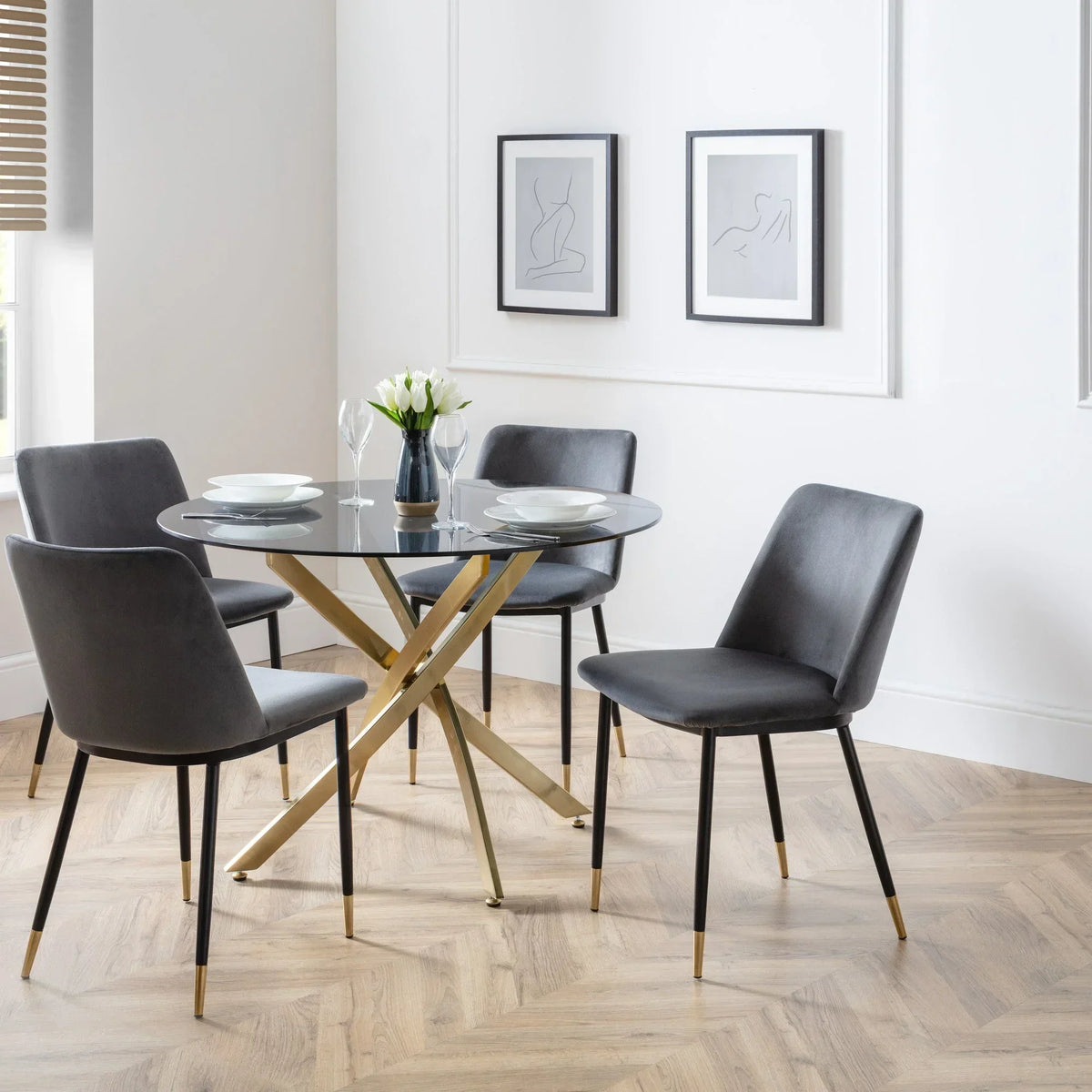 Glass dining table with gold metal legs and four grey velvet chairs in modern dining room