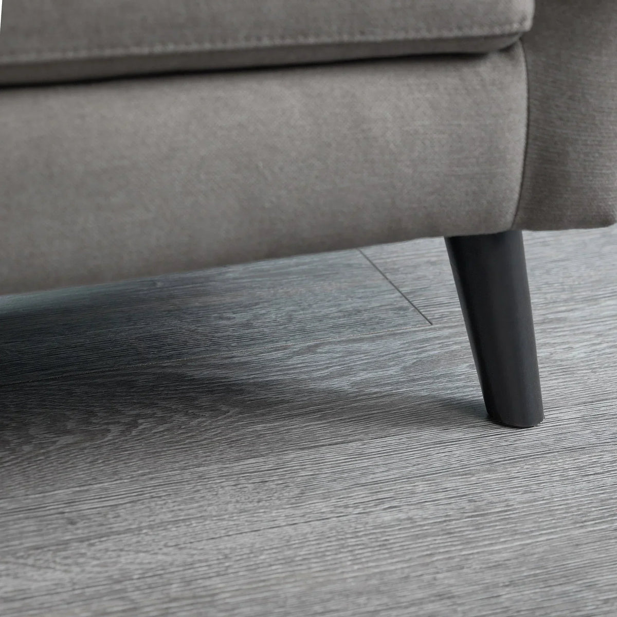 Grey fabric sofa leg detail on wood floor, highlighting upholstery and leg finish