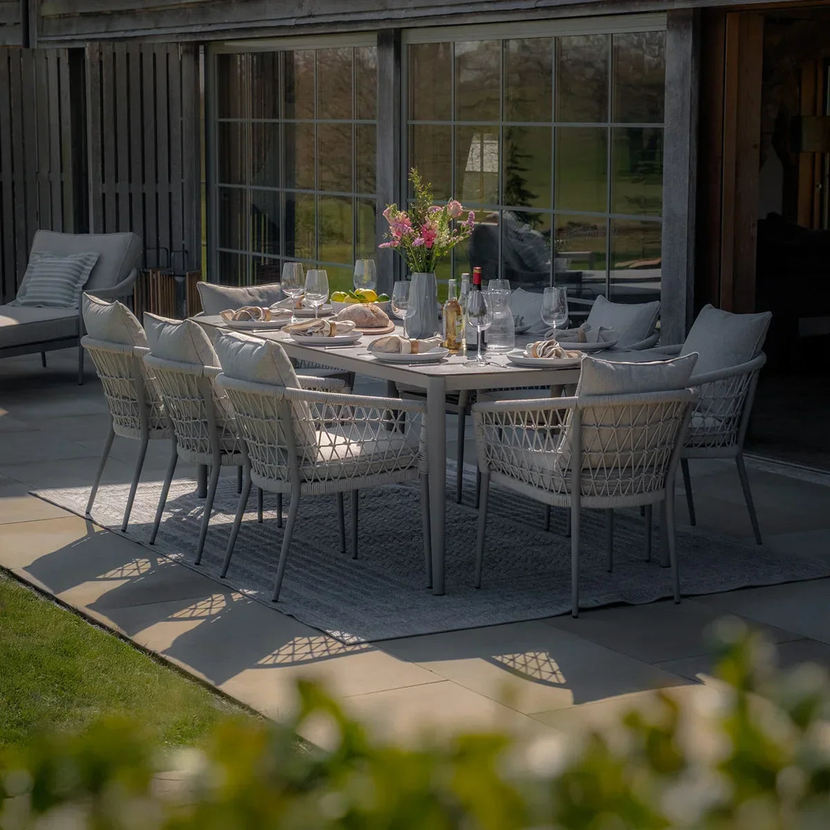 Grey outdoor dining set with woven chairs and cushions set for a meal on a patio
