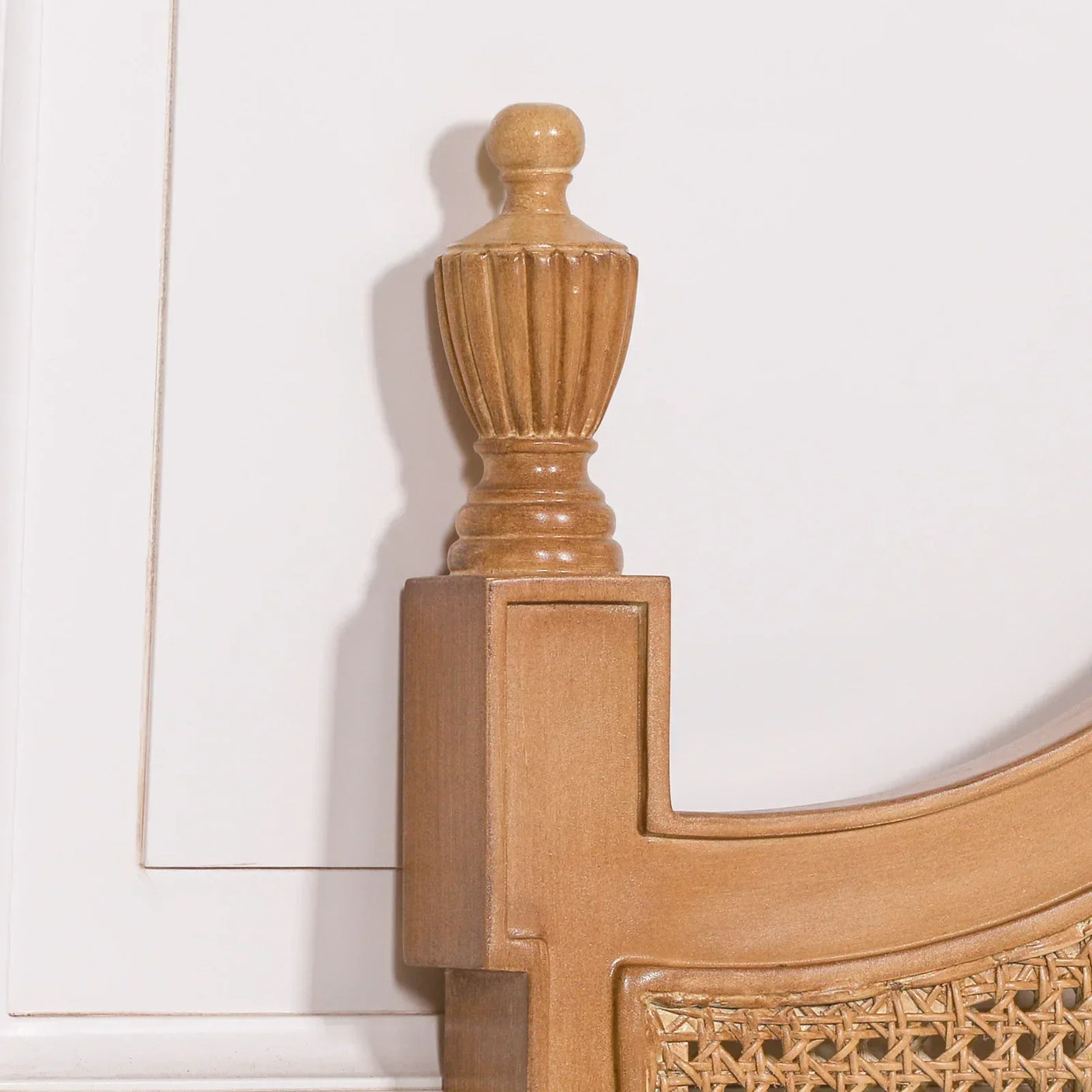 Carved oak bed frame corner with decorative finial and woven rattan headboard detail