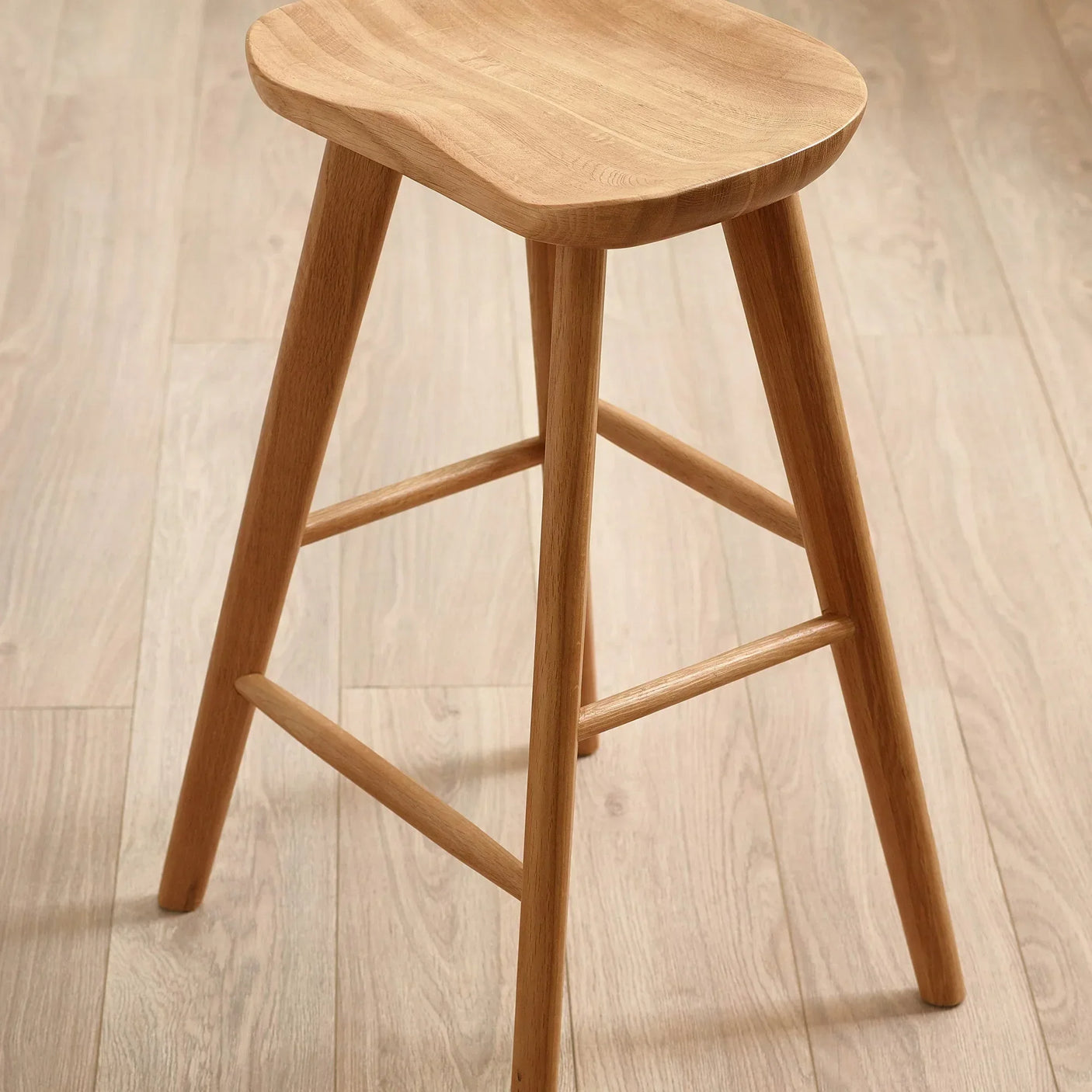 Wooden bar stool with curved seat and angled legs on light hardwood floor