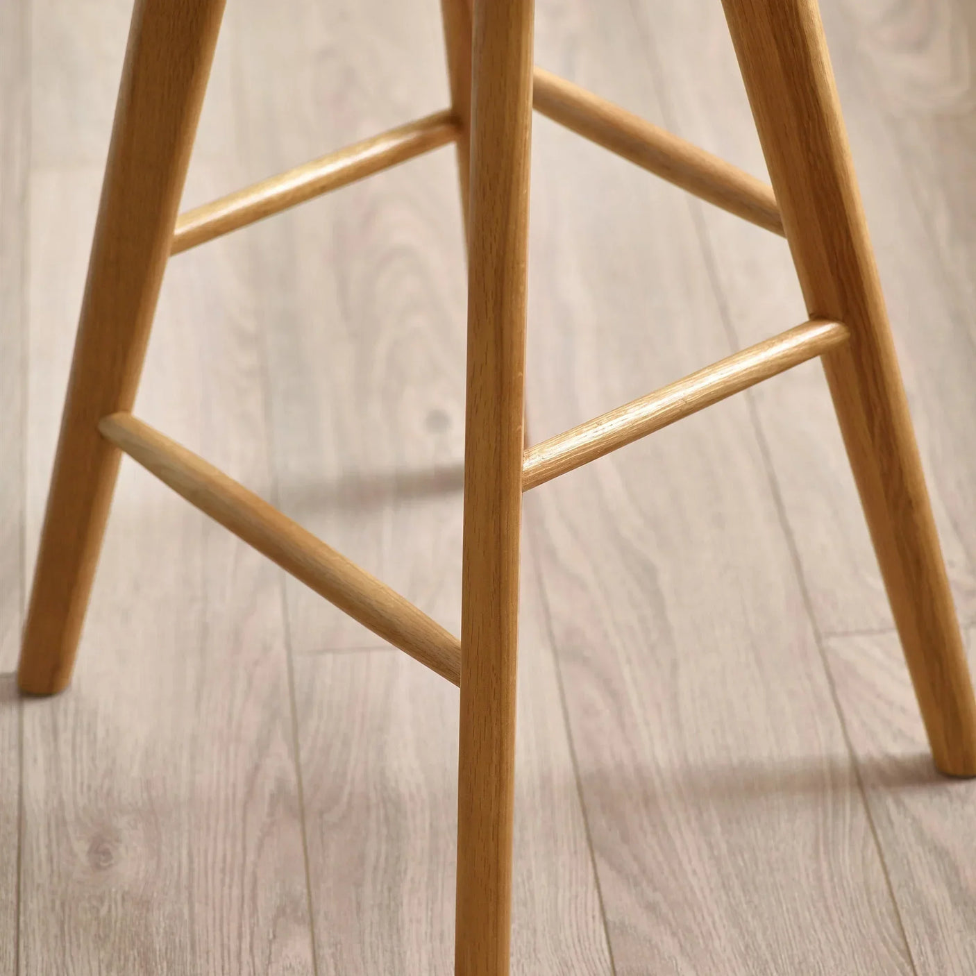 Light oak wooden stool legs with cross braces on light wood floor