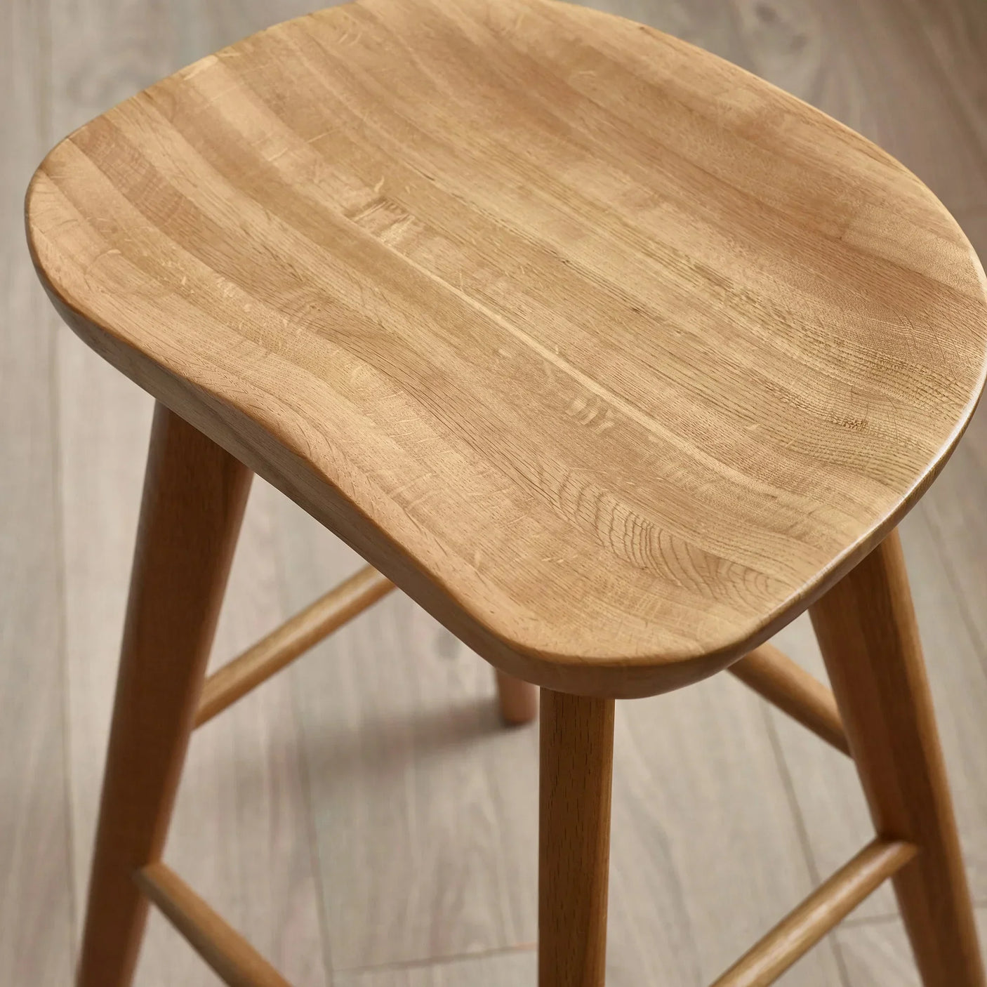 Solid wood bar stool with natural finish and curved seat on light wooden floor