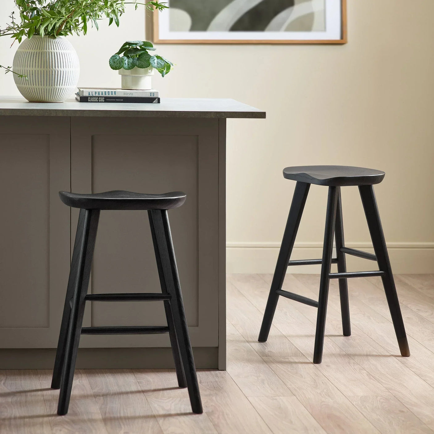 Black wooden bar stools with contoured seats next to a modern kitchen island on wood flooring