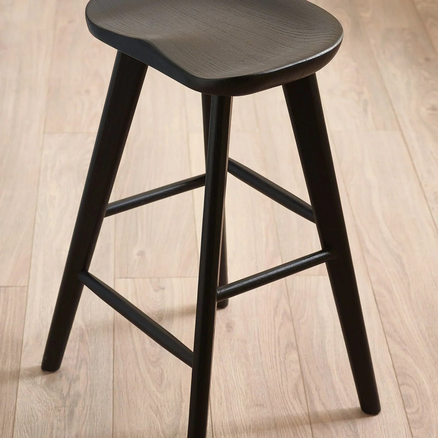 Black wooden bar stool with contoured seat and angled legs on light wood floor