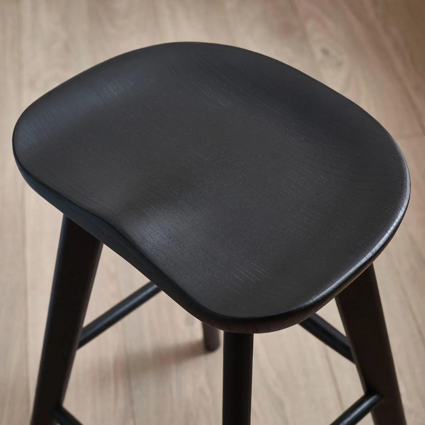 Black wooden bar stool with curved seat viewed from above on light wood floor