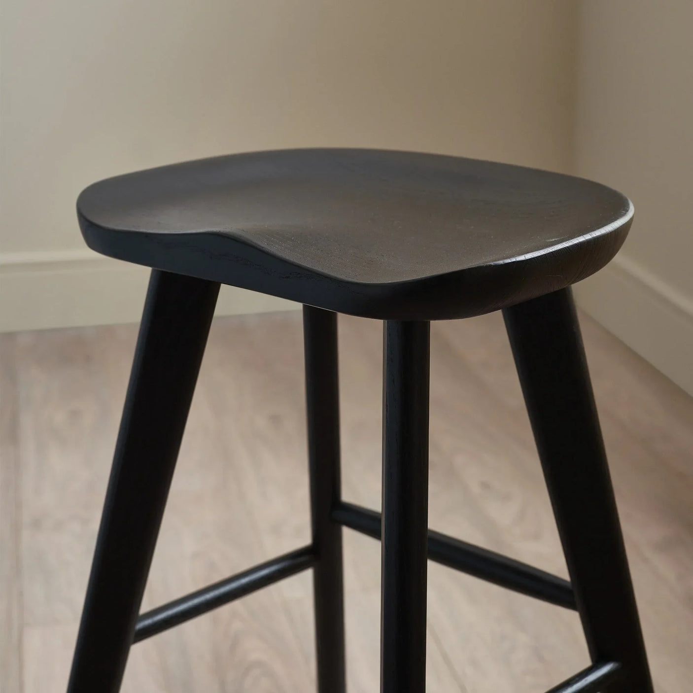 Black wooden bar stool with contoured seat and angled legs on light wood floor